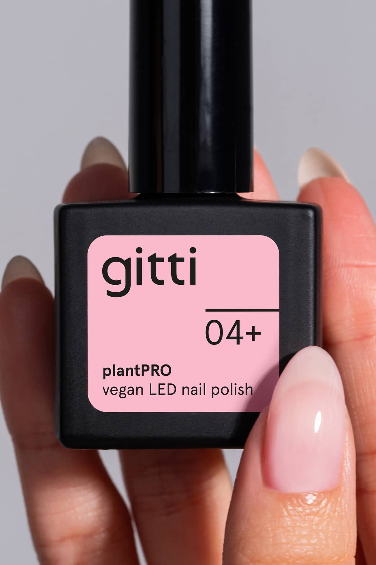 Eine Hand hält eine Flasche des veganen LED-Nagellacks von gitti plantPRO System + Lamp mit der Aufschrift 04+, mit hellrosa Lack auf den Fingernägeln - ideal für die Verwendung mit der plantPRO System + Lamp.