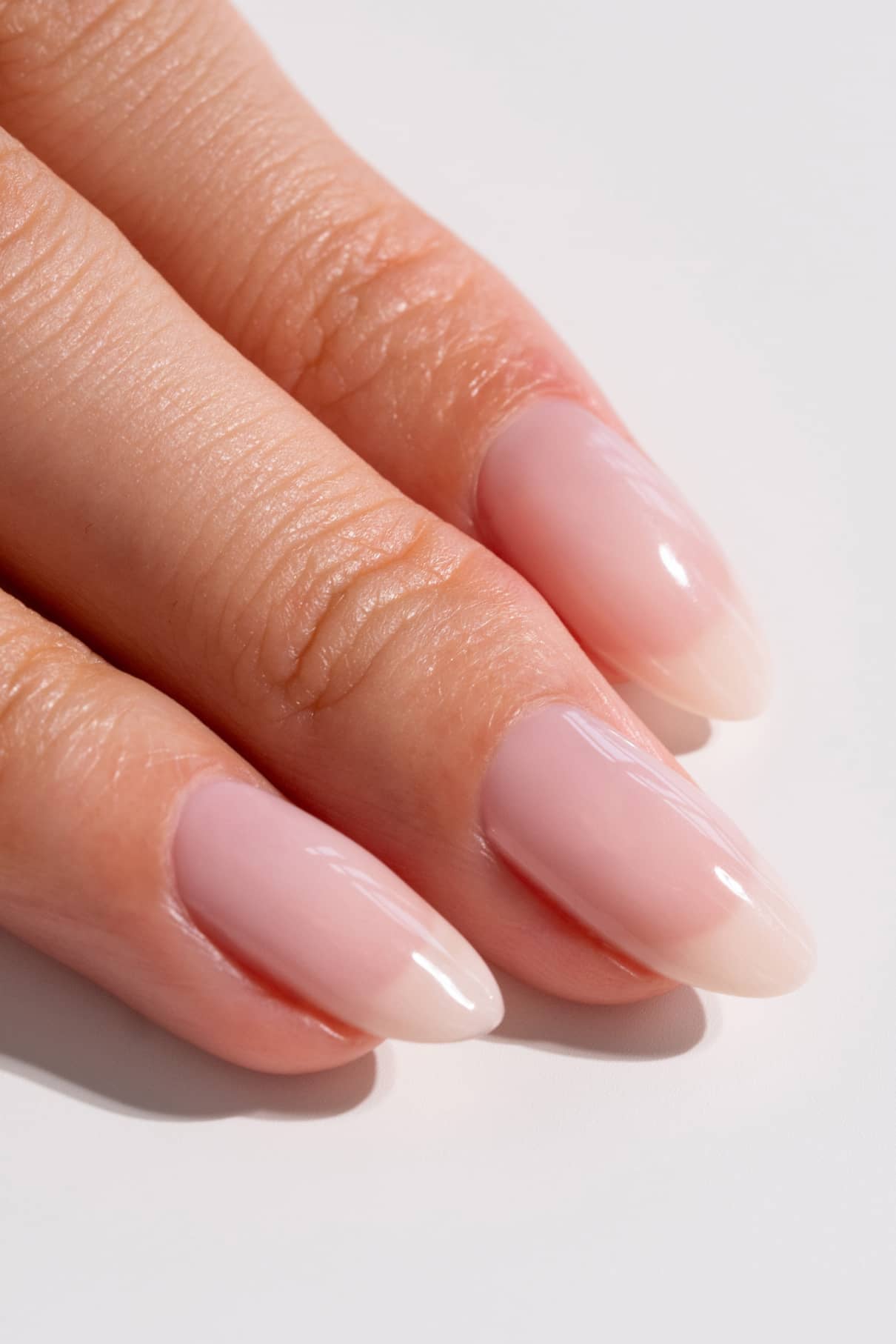 Nahaufnahme einer Hand mit drei Fingern, jeder mit langen, mandelförmigen Nägeln, die in gitti no. 04+, einem glänzenden Nude-Ton in zartem Rosa.