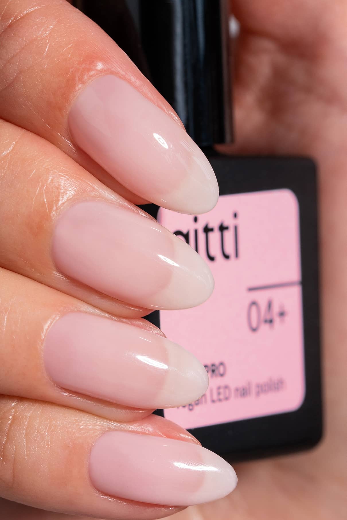 Nahaufnahme einer Hand mit langen, mandelförmigen, zartrosa lackierten Nägeln, die eine Flasche mit LED-Nagellack mit der Aufschrift gitti no. 04+.