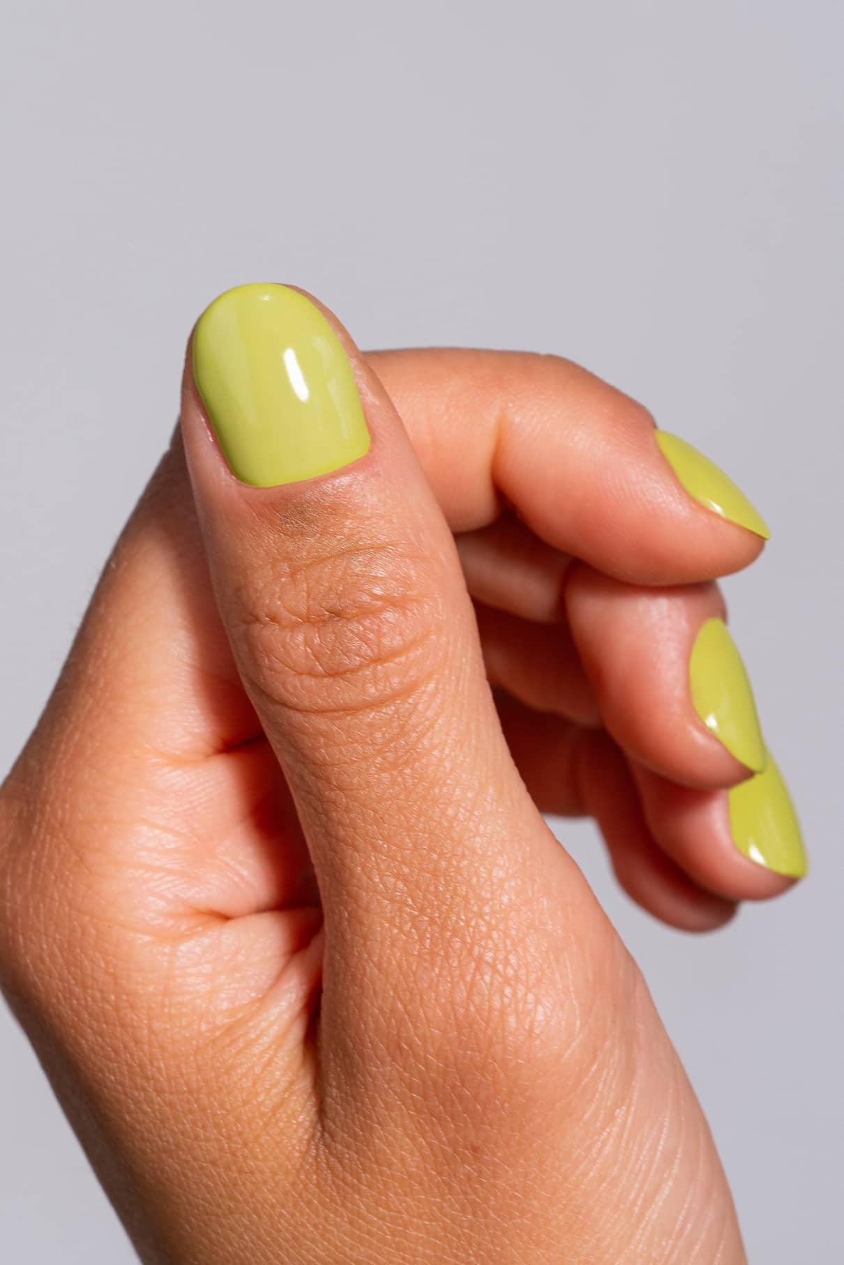 Eine Hand mit kurzen, sauber manikürten Nägeln, lackiert in gitti no. 05+, einem glänzenden, modernen Grün mit gelbem Unterton, vor einem neutralen Hintergrund.