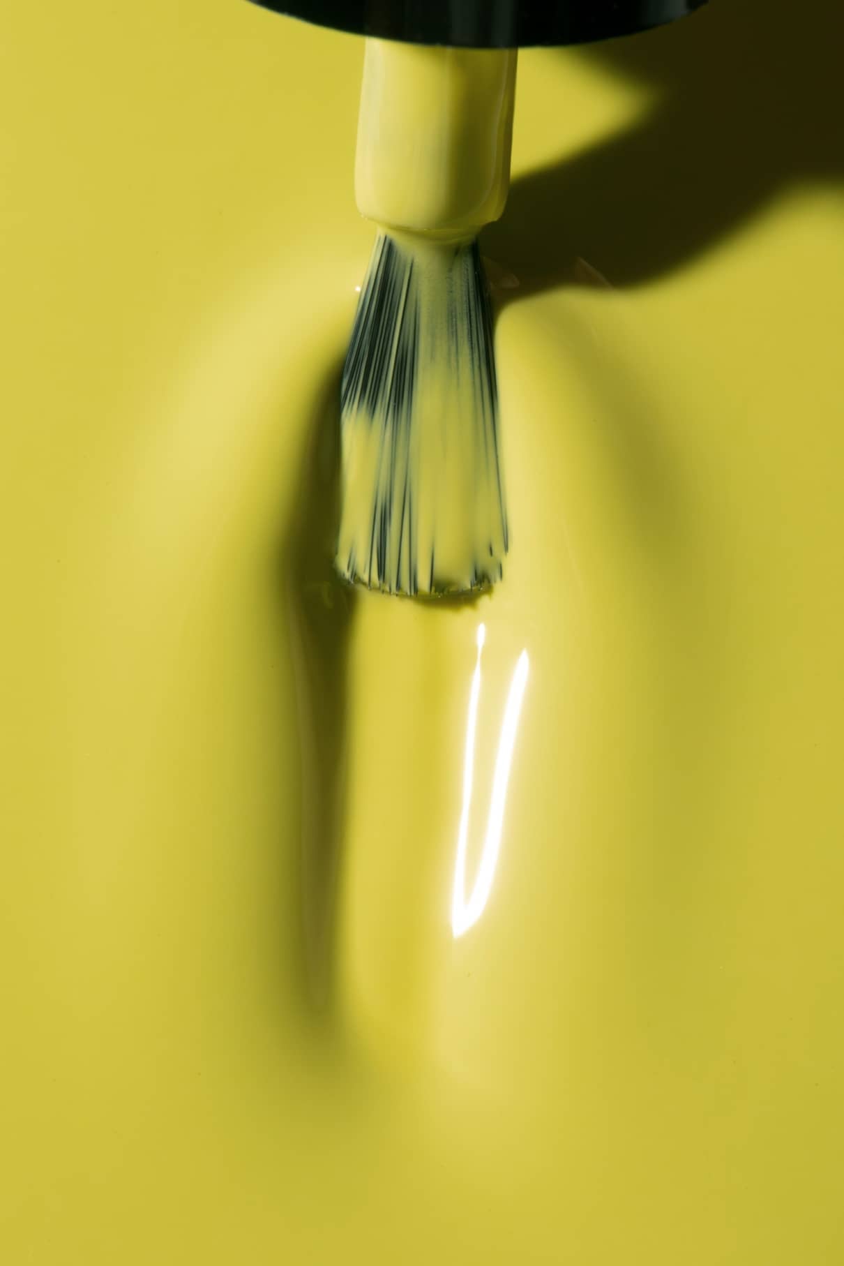 Nahaufnahme eines Pinsels, der gitti no. 05+, ein glänzender, moderner grüner Nagellack mit einem gelben Unterton, auf eine glatte Oberfläche, wobei die sichtbaren Borsten und das reflektierte Licht hervorgehoben werden.