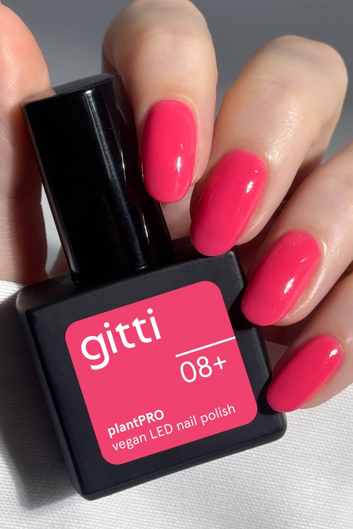 Eine Hand mit strahlenden Pink-Nägeln hält eine Flasche gitti no. 08+ plantPRO vegan LED Nagellack.