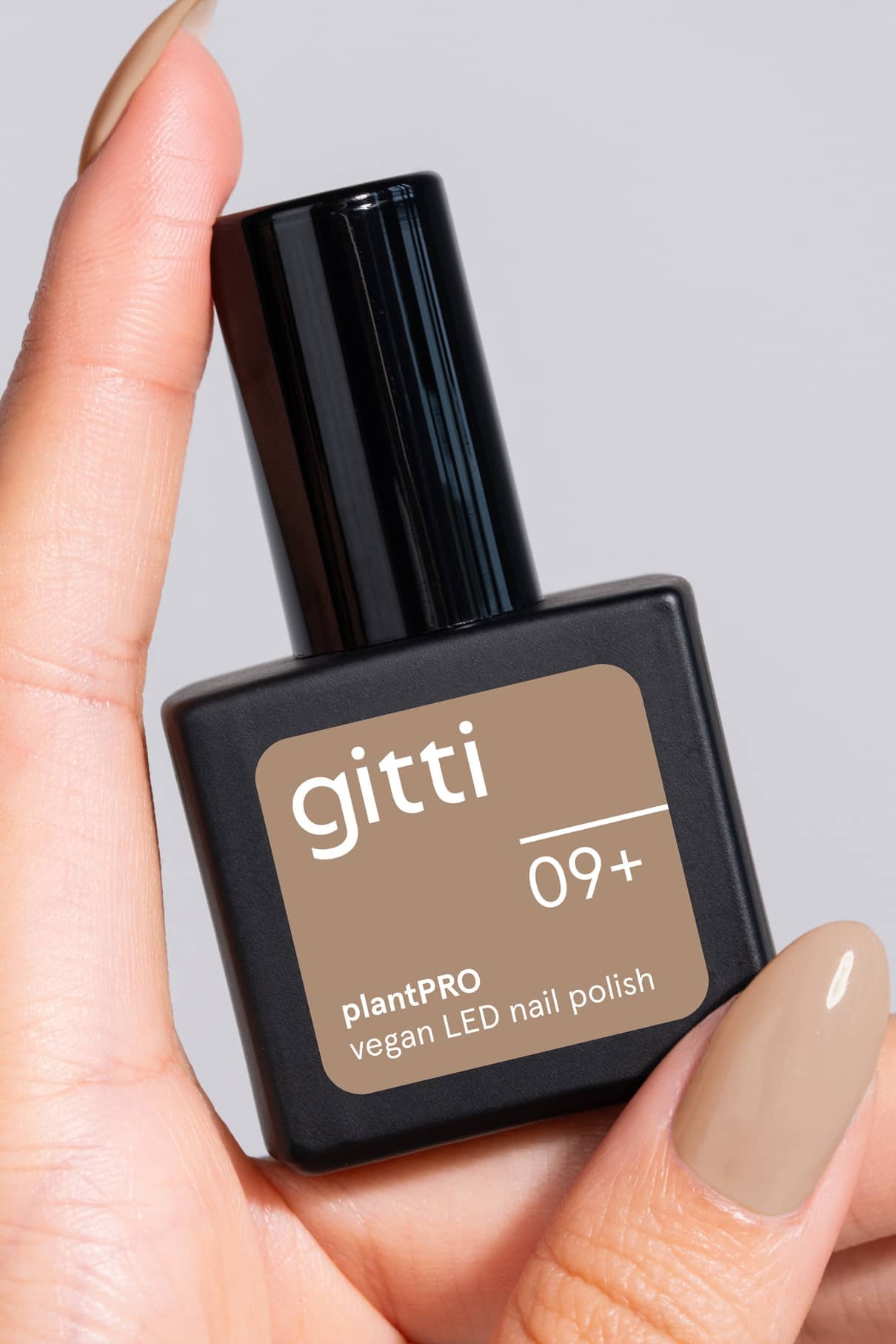 Eine Hand hält eine Flasche gitti plantPRO System + Lamp veganen LED-Nagellack in der Farbe 09+ mit passenden beigen Nägeln - ideal für die Verwendung mit Ihrer Gel-Nagellampe oder als Teil Ihres Gel-Nagel-Systems.