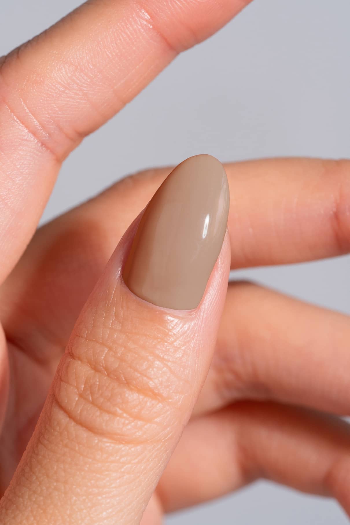 Nahaufnahme einer Hand mit einem sauber manikürten Daumennagel, der in dem glänzenden, warm getönten hellen Braunton gitti no. 09+.