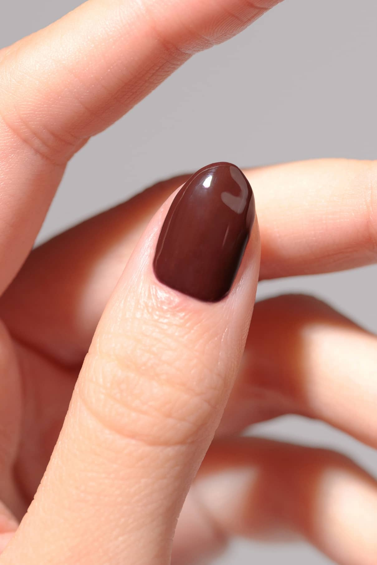 Nahaufnahme einer Hand mit kurzen, glänzenden Nägeln, lackiert in gitti no. 10+, einem dunklen Beerenton, vor einem neutralen Hintergrund.