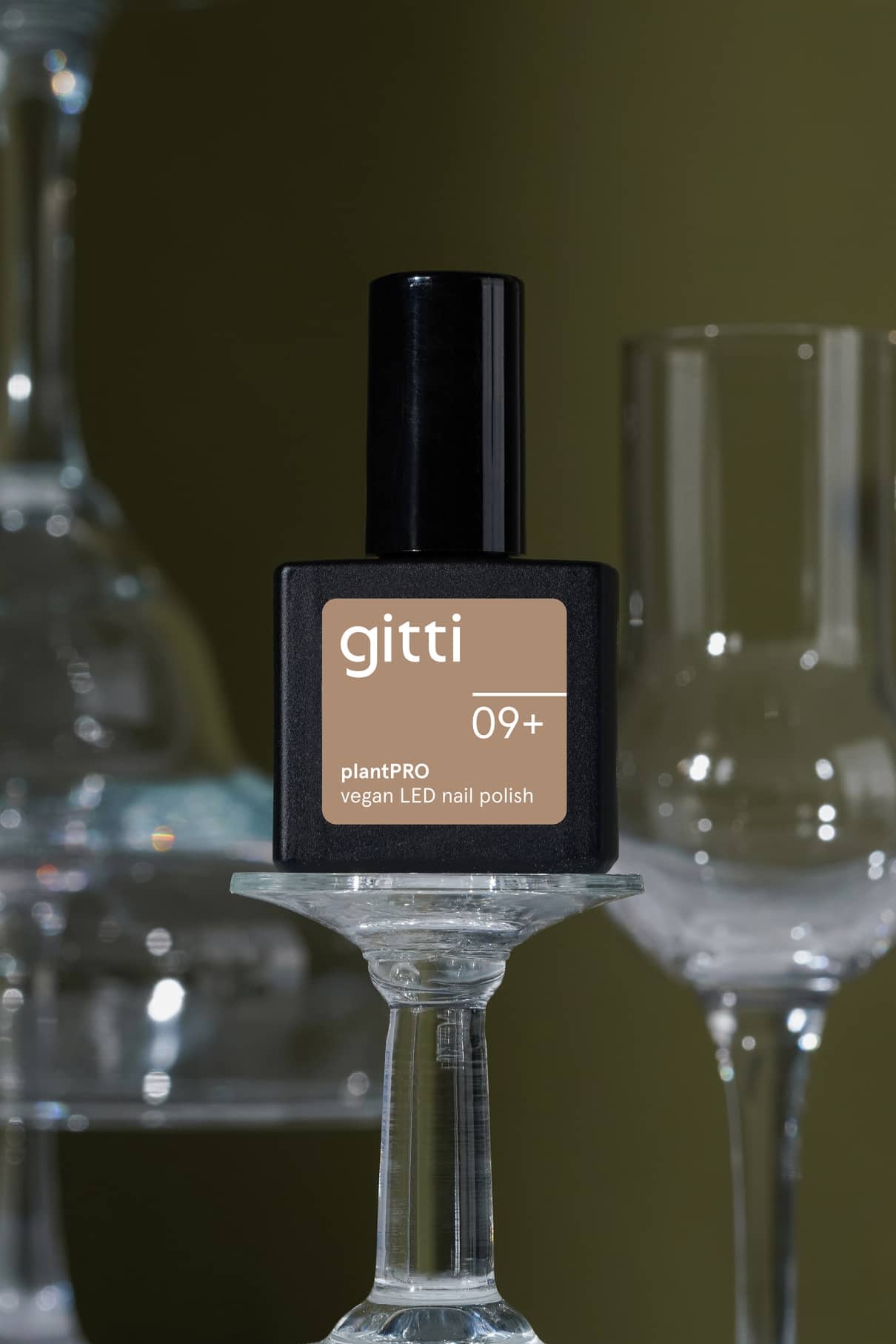 Eine Flasche gitti no. 09+ veganer LED-Nagellack in der Farbe 09+, einem hellen Braun mit warmen Untertönen, ruht auf einem umgedrehten Weinglas, wobei weitere Gläser im Hintergrund verschwimmen.
