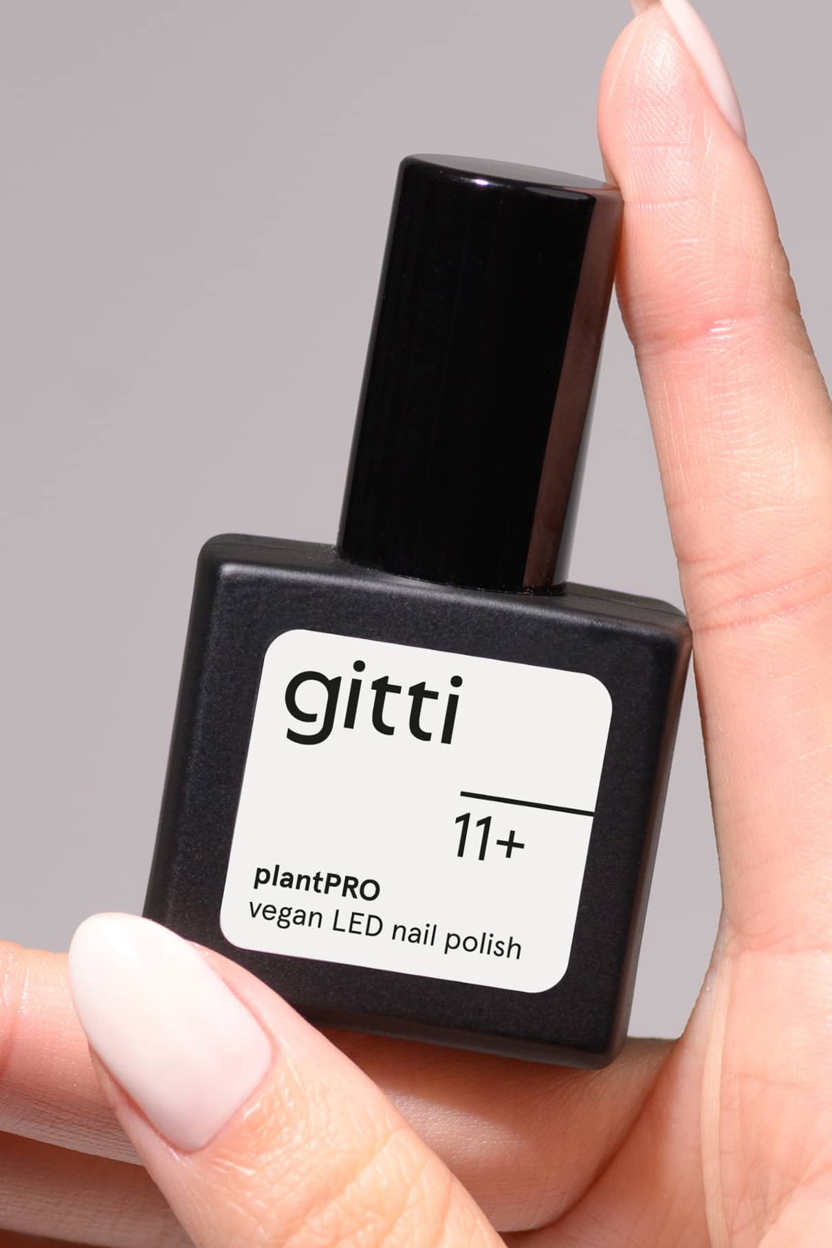 Eine Hand mit manikürten Nägeln hält ein schwarzes Fläschchen aus dem plantPRO System + Lampe, einem veganen LED-Nagellack, der perfekt für jedes Gel-Nagel-System geeignet ist und mit Ihrer Lieblings-Gel-Nagellampe funktioniert.