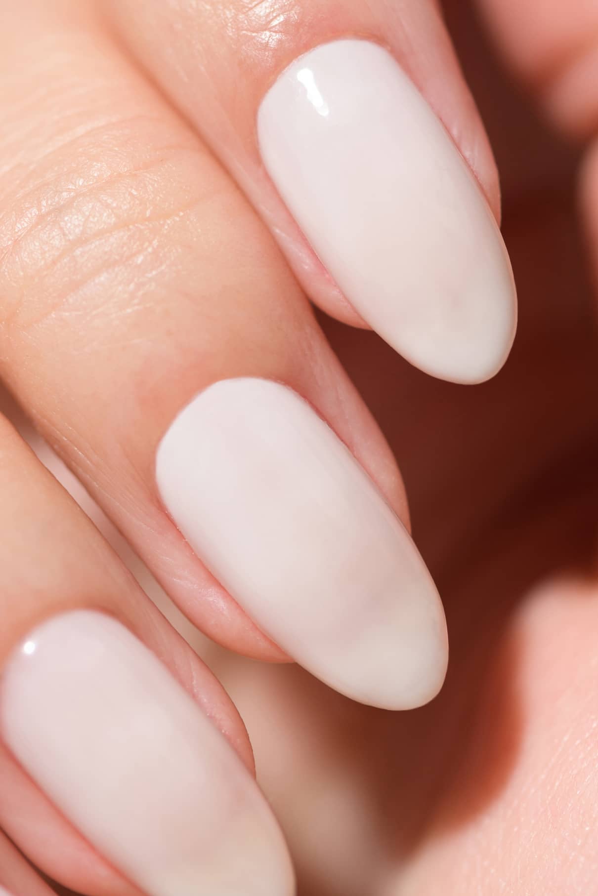 Nahaufnahme einer Hand mit mandelförmigen Naturnägeln, die mit glänzendem, halbtransparentem gitti no. 11+ in zartem Weiß oder Hellrosa.