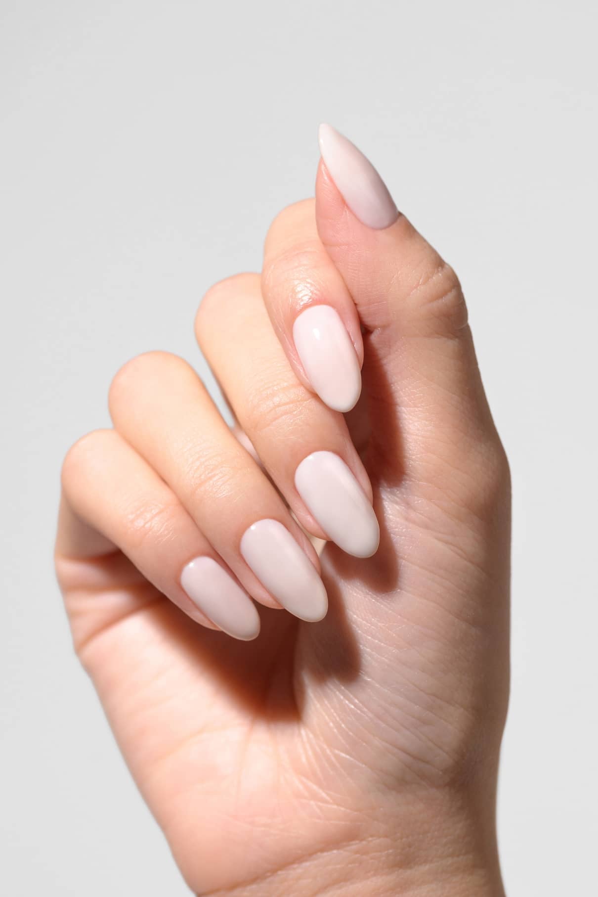 Eine Hand mit langen, mandelförmigen Nägeln, die in dem zarten, milchig-weißen Farbton gitti no. 11+ zeigt ein halbtransparentes Nageldesign vor einem schlichten, hellen Hintergrund.