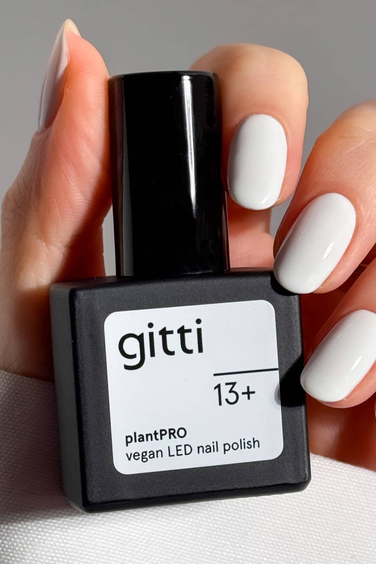 Eine Hand mit weiß lackierten Nägeln hält eine schwarze Flasche des veganen LED-Nagellacks gitti PRO Colour Trio, der Teil des plantPRO Farben Sets ist.