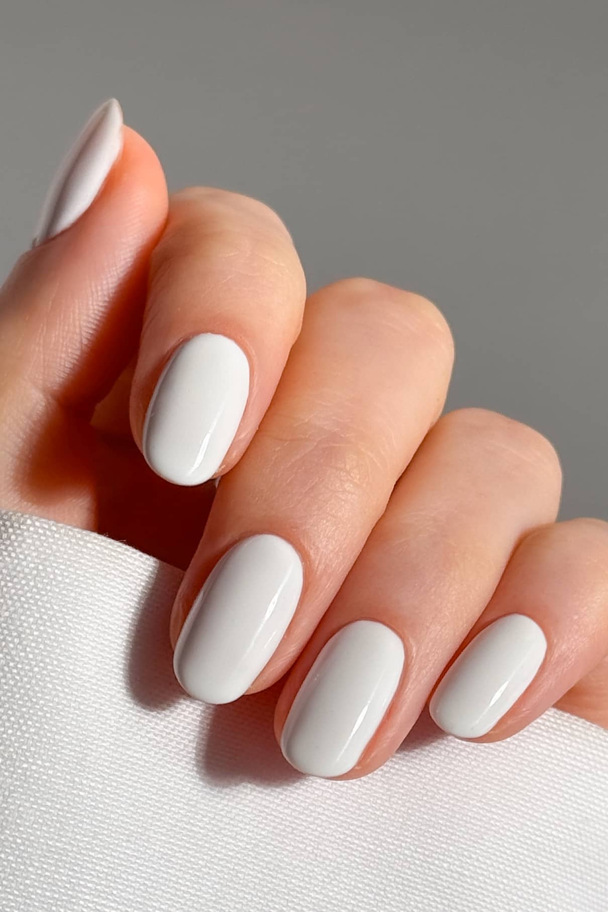 Eine Hand mit kurzen, ovalen Nägeln, die mit gitti no. 13+ lackierten Nägeln hält ein Stück weißen, strukturierten Stoff vor einem neutralen Hintergrund.