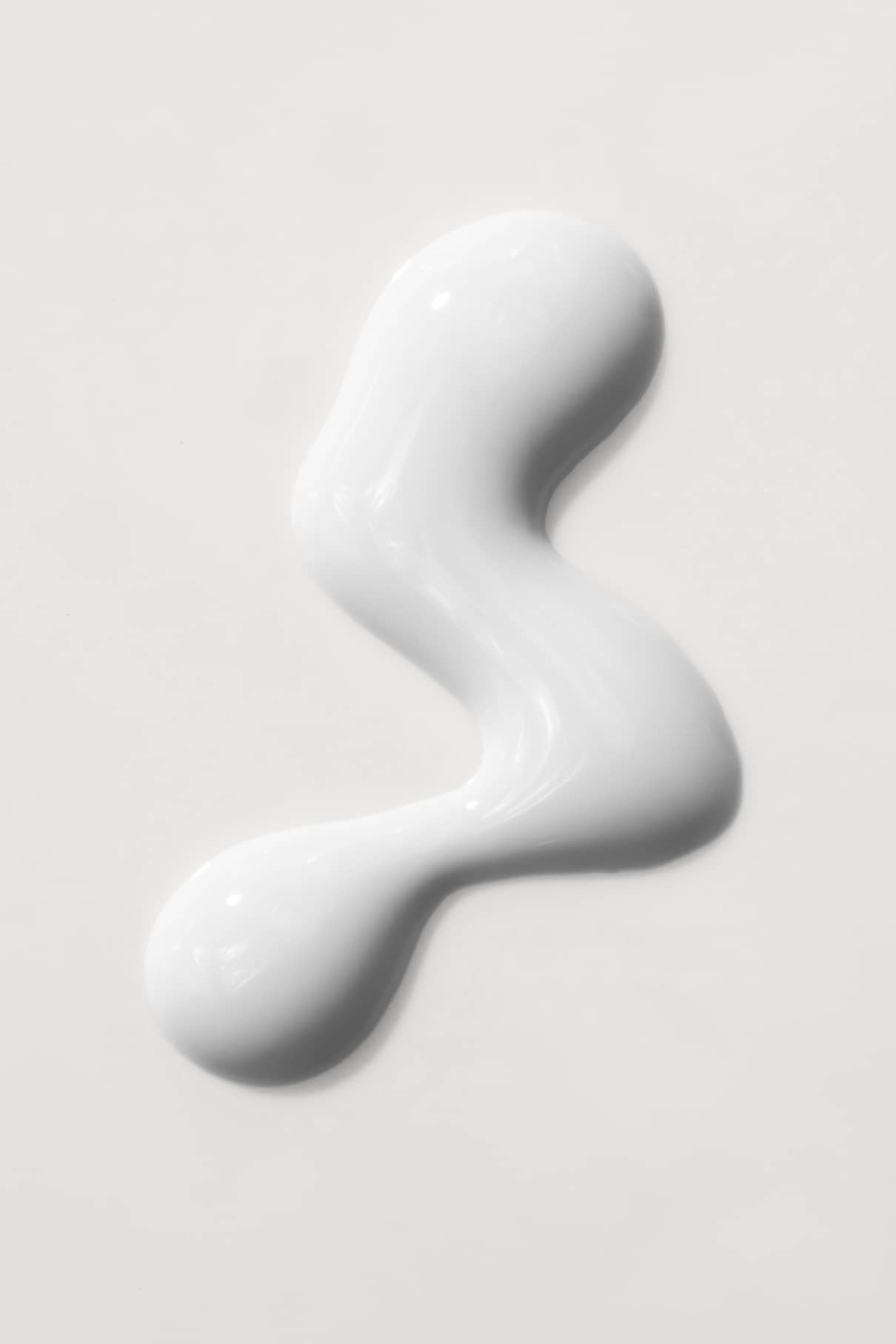 Eine weiße, cremige Flüssigkeit von gitti no. 13+ wird in einer unregelmäßigen, geschwungenen Form auf einer glatten weißen Fläche verteilt.