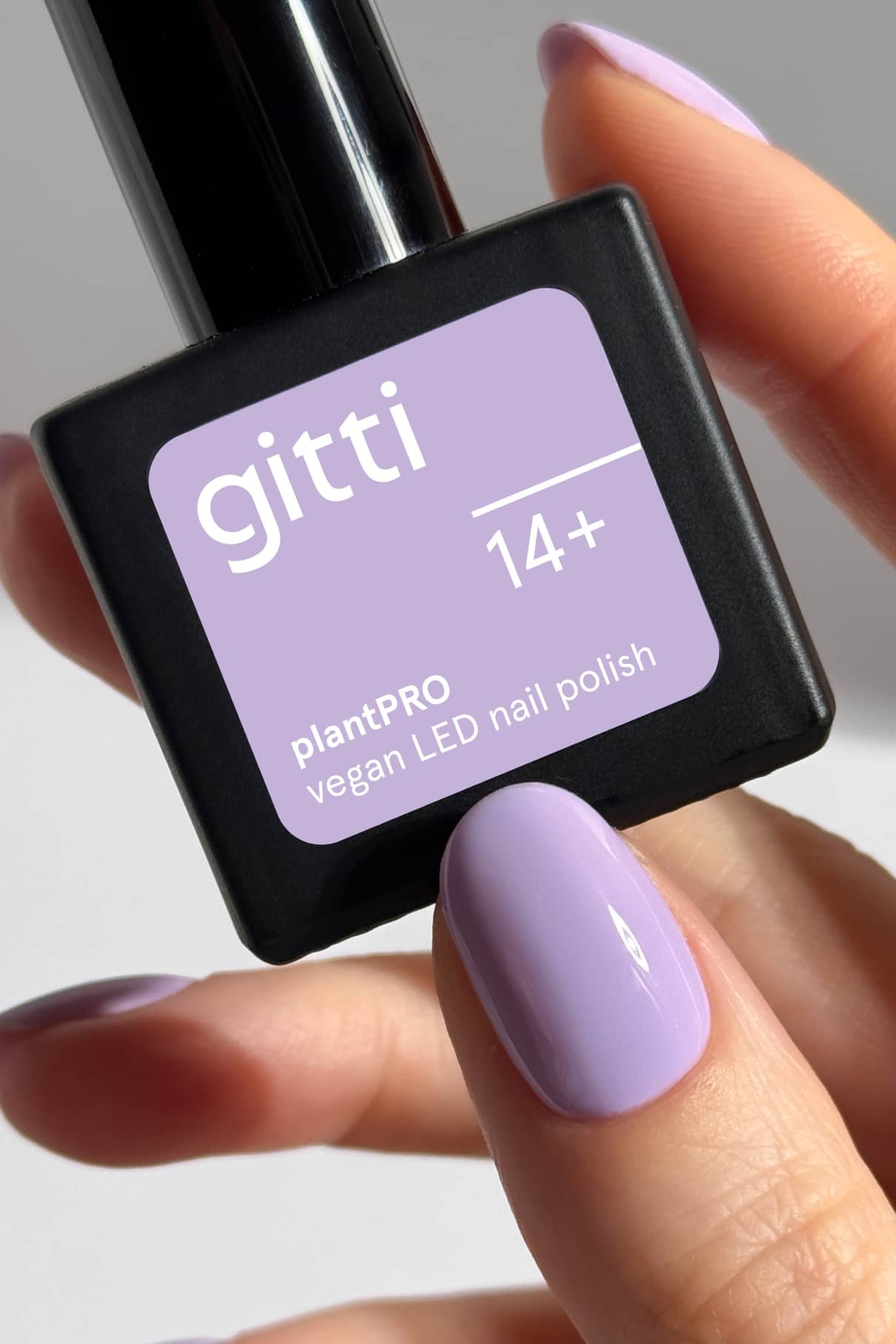 Eine Hand mit hellviolett lackierten Nägeln in einem intensiven Lavendel-Ton mit kühlem Unterton hält eine Flasche gitti no. 14+ plantPRO vegan LED Nagellack in einer passenden Farbe.