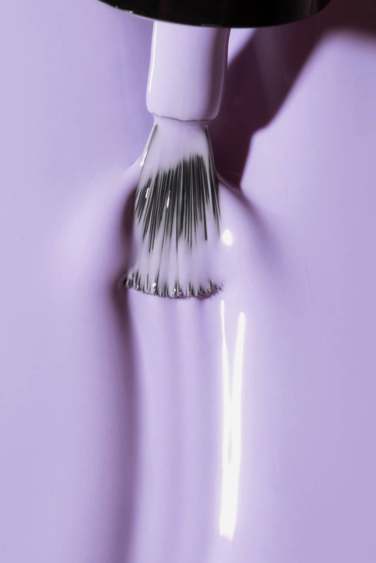 Nahaufnahme eines Nagellackpinsels, der den glänzenden, intensiven gitti no. 14+ Lavendel Nagellack mit kühlem Unterton auf eine glatte Oberfläche auf.