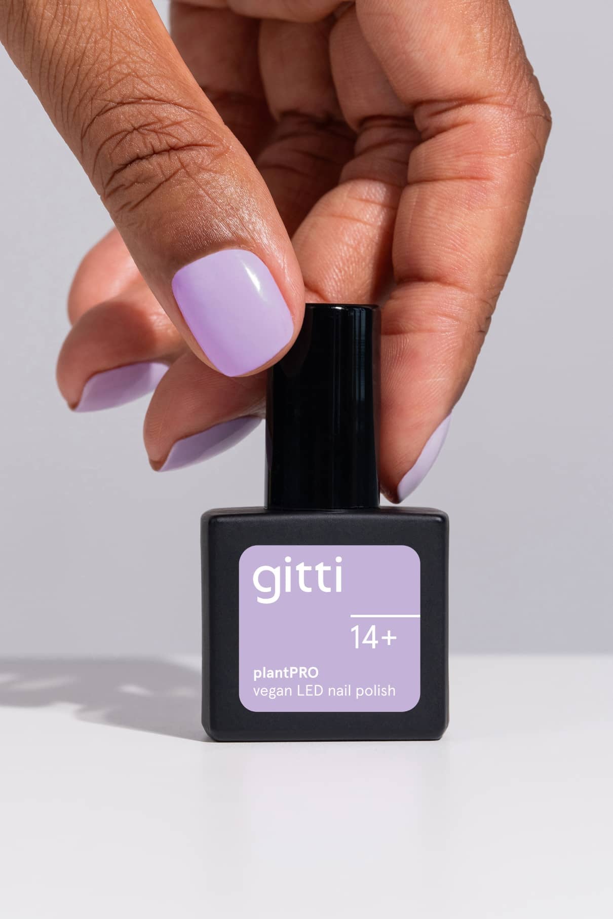 Eine Hand mit lavendelfarbenen Nägeln hält eine quadratische Flasche des veganen LED-Nagellacks gitti PRO Colour Trio in einem passenden Lavendelton.