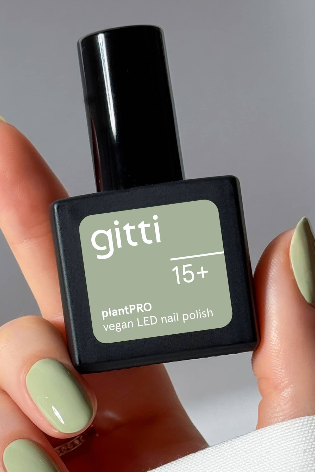 Eine Hand mit salbeigrünen Nägeln hält eine Flasche des veganen LED-Nagellacks PRO Colour Trio mit der Aufschrift 15+.