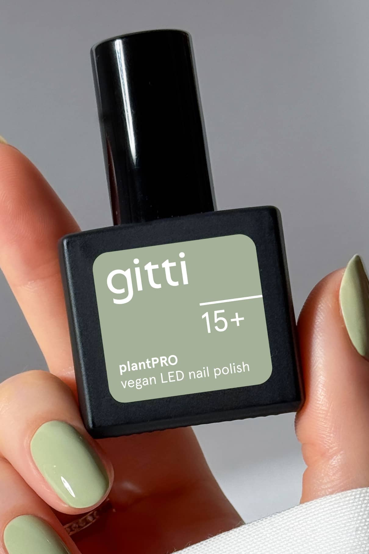 Eine Hand mit salbeigrünen Nägeln hält eine Flasche des veganen LED-Nagellacks PRO Colour Trio mit der Aufschrift 15+.