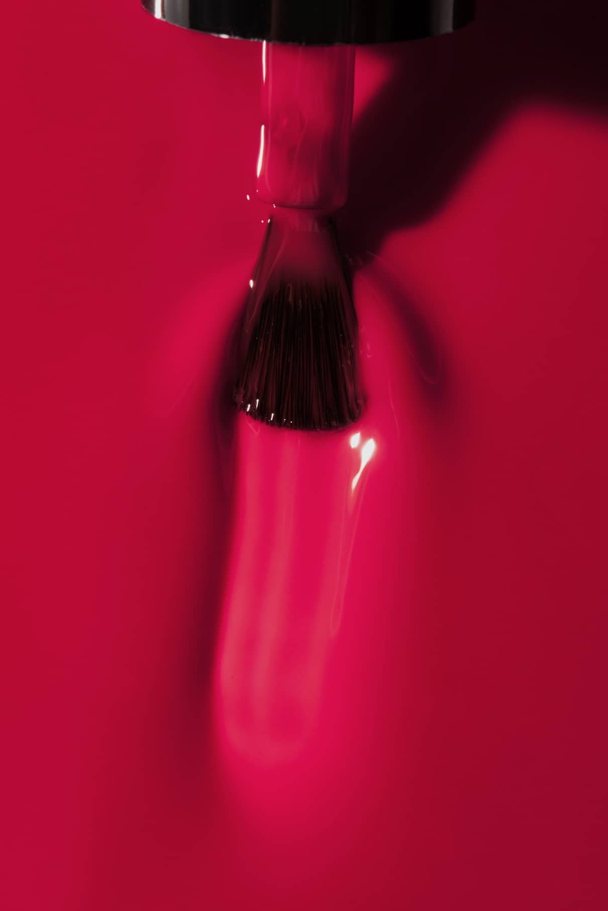 Eine Nahaufnahme eines gitti no. 16+ Nagellackpinsel, der glänzende, beerenrosa Farbe auf einen glatten roten Hintergrund aufträgt.