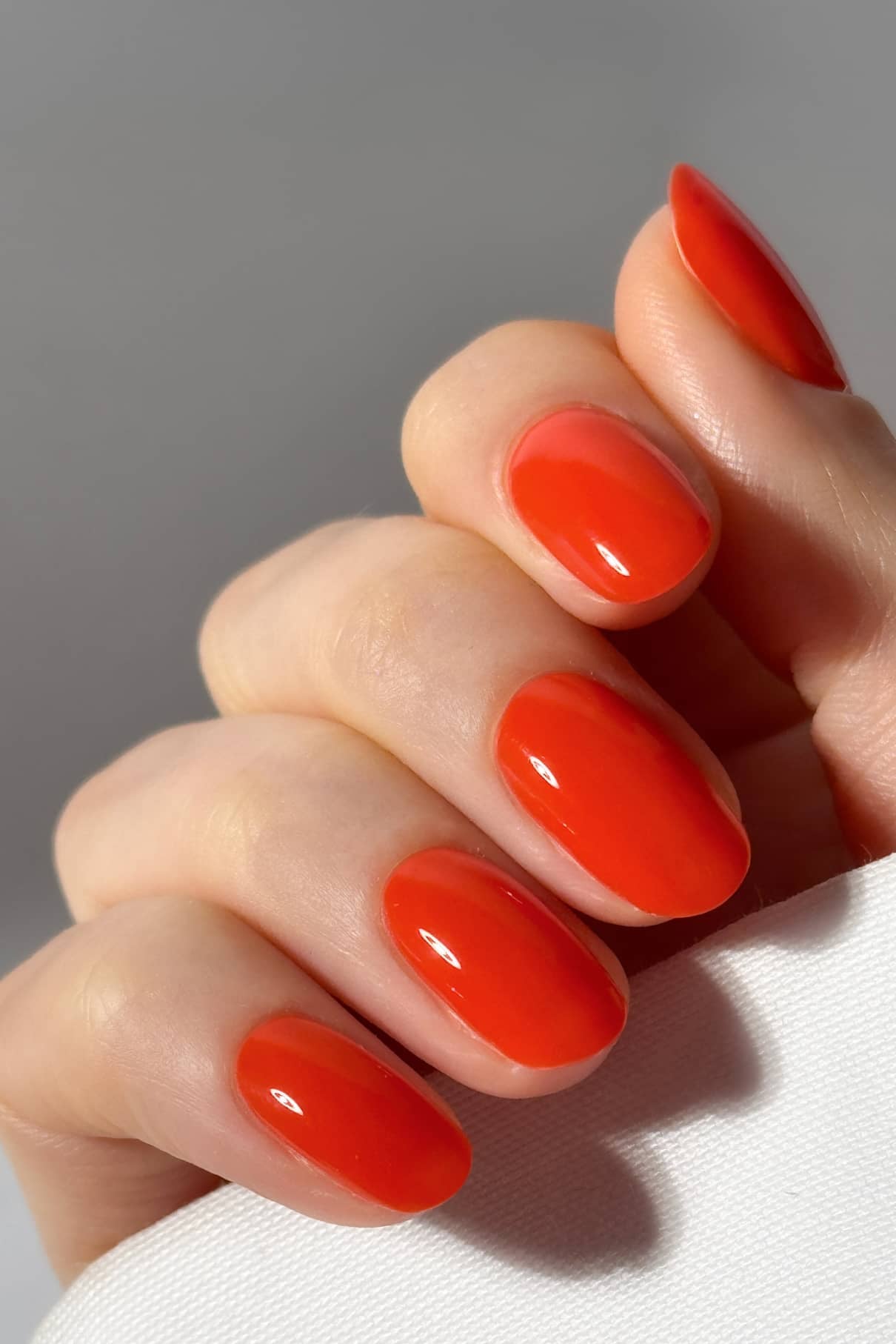 Eine Hand mit kurzen, ovalen Nägeln, lackiert in der glänzenden, intensiv orangeroten Farbe gitti no. 18+.
