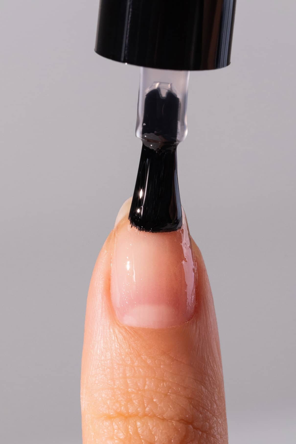 Nahaufnahme einer Person, die mit einem Pinsel schwarzen Nagellack über einem plantPRO Base Coat auf ihren Fingernagel aufträgt.