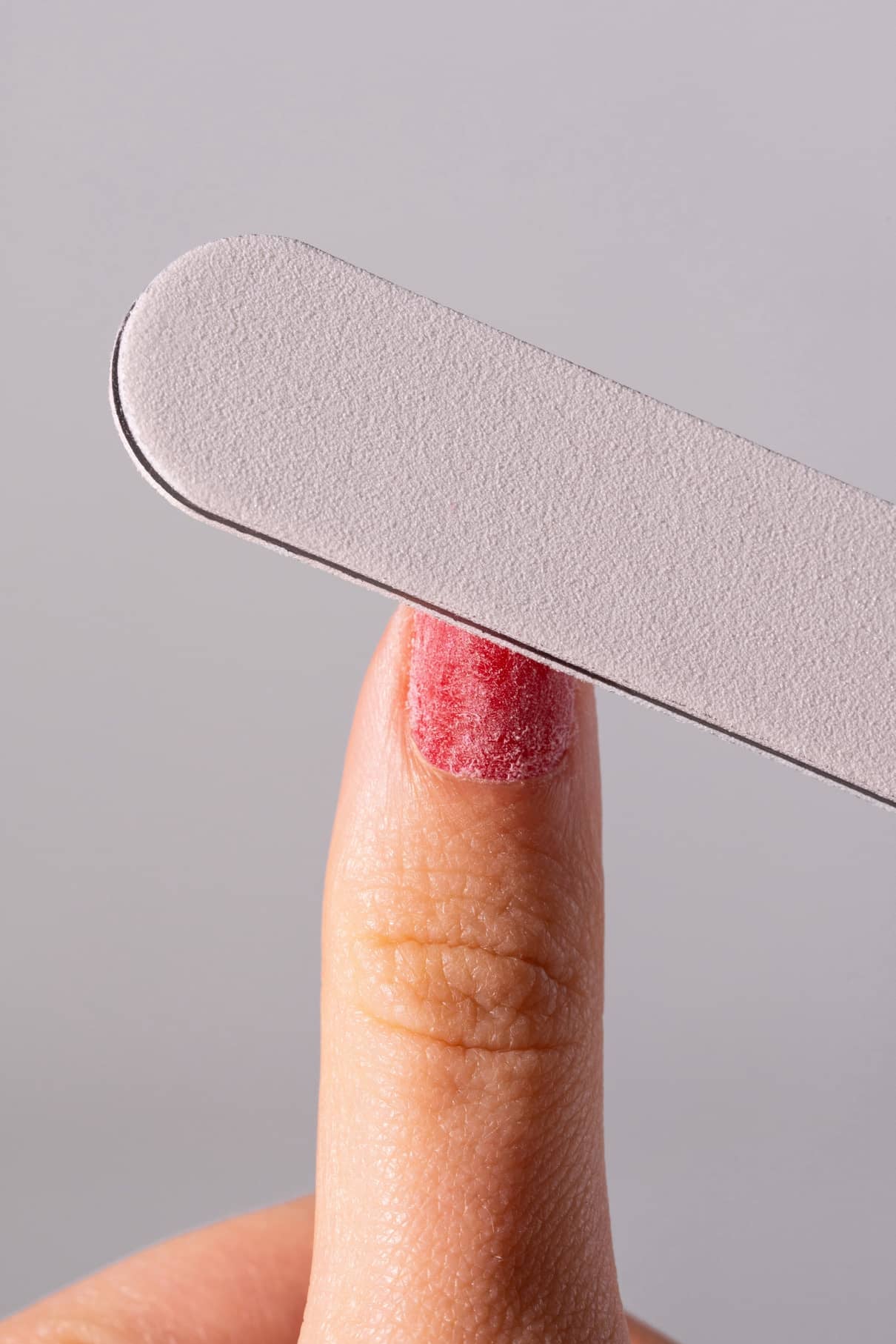 Nahaufnahme eines Fingernagels mit teilweise entferntem roten Lack, der mit dem PRObuffer, einer grauen Nagelfeile 100/240, gefeilt wurde.
