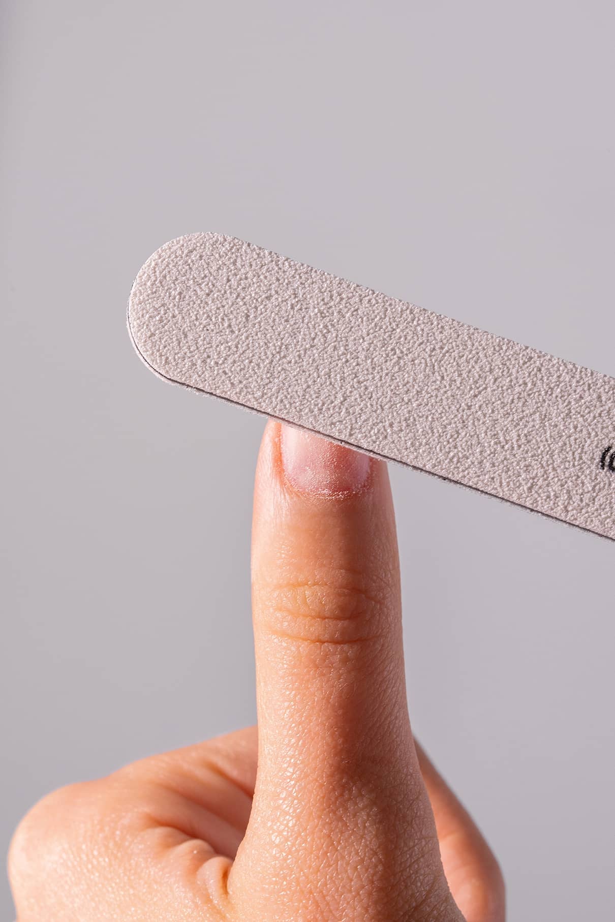 Eine Hand hält einen Zeigefinger hoch, während ein PRObuffer 100/240 Nagelpuffer vor einem unifarbenen Hintergrund über den Fingernagel gelegt wird.