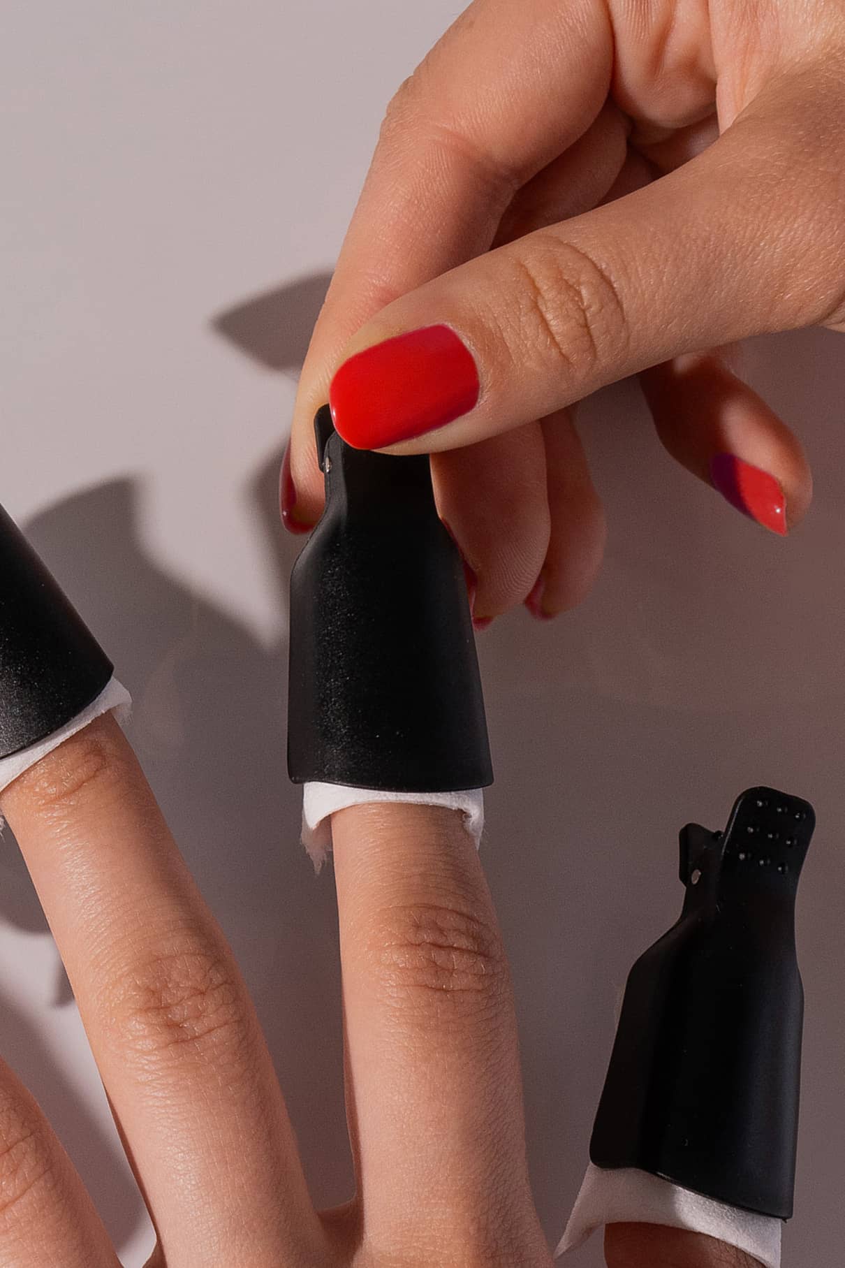 Eine Hand mit rotem Nagellack entfernt einen PROclips vom Finger; weitere Finger tragen ebenfalls PROclips und Wattepads für eine effektive Nagelpflege mit Nagellackentferner.