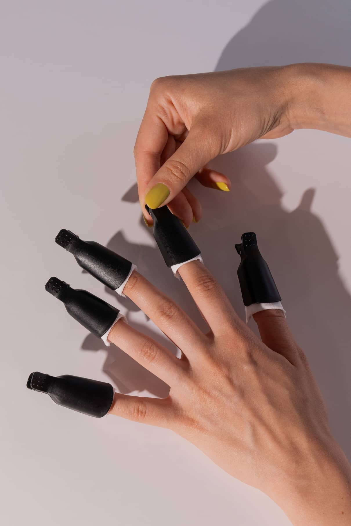 Eine Hand mit gelbem Nagellack setzt einen schwarzen PROclips-Entferner-Clip auf einen anderen Finger, an dem bereits vier PROclips angebracht sind, für eine einfache und gründliche Nagelpflege.