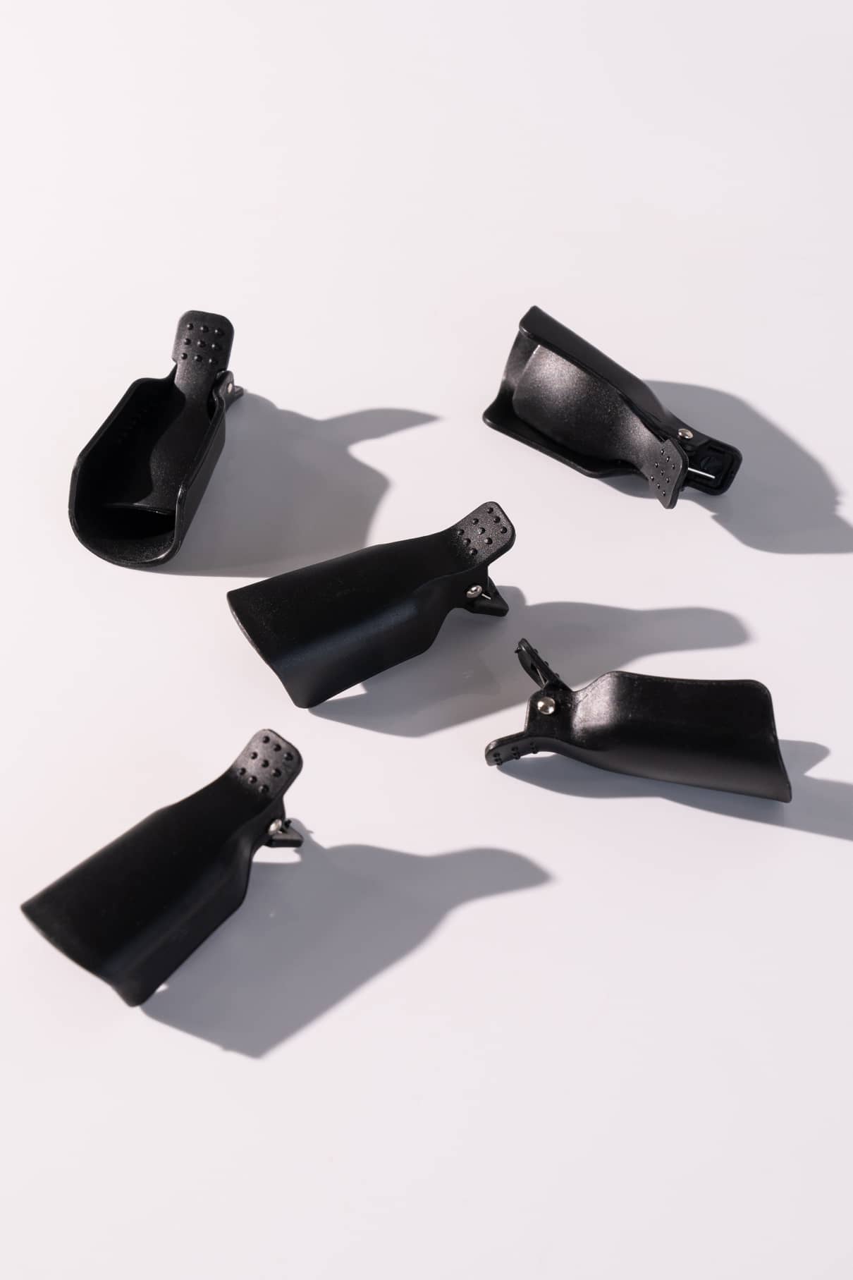 Fünf schwarze PROclips für die Nagelpflege sind auf einer hellen Fläche angeordnet und werfen jeweils einen deutlichen Schatten.