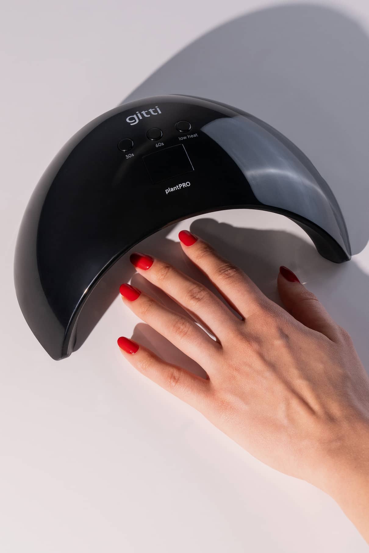 Eine Hand mit rot lackierten Nägeln wird unter der schwarzen plantPRO System + Lampe auf eine hellgraue Fläche gelegt.