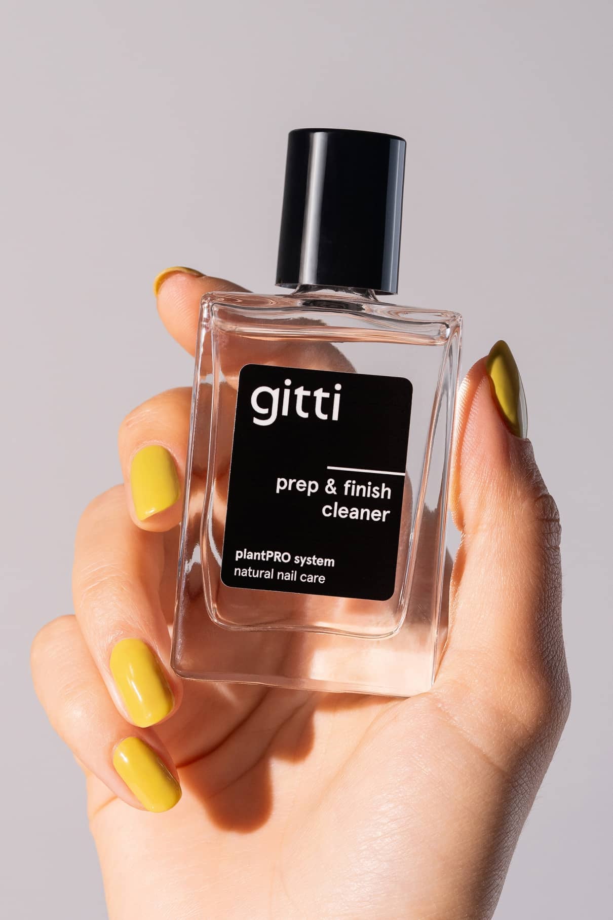 Eine Hand mit gelb lackierten Nägeln hält eine durchsichtige Flasche mit der Aufschrift plantPRO Refill Set, Naturnagelpflege - ideal zum Vorbereiten vor dem Base Coat oder zum Entfernen des Lacks mit dem Soak-off Remover, alles vor einem schlichten Hintergrund.