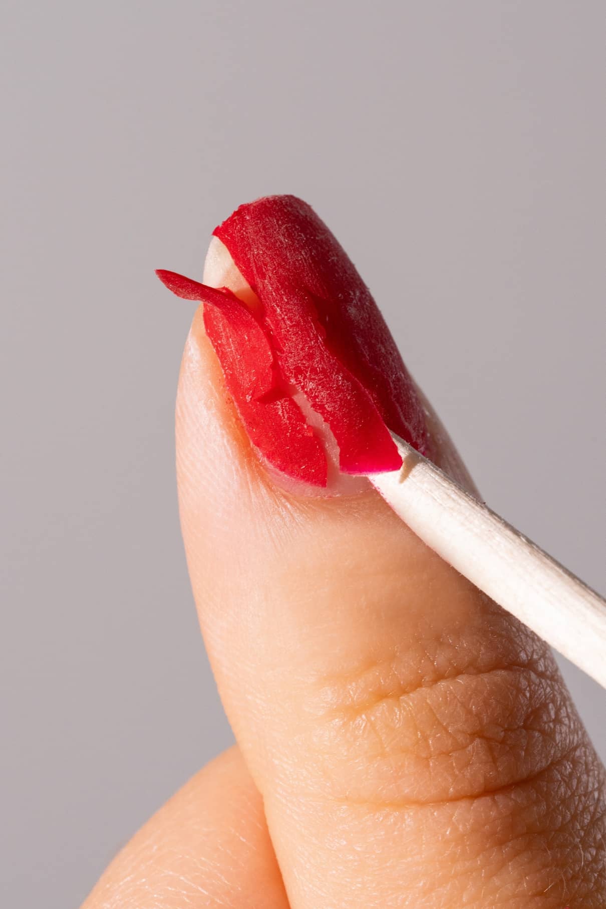 Eine Nahaufnahme eines Daumens mit rotem Nagellack, der mit PROsticks, Manikürestäbchen aus unbehandeltem Birkenholz, abgezogen wird.