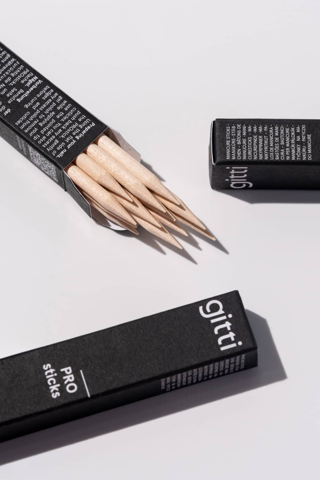 In einer geöffneten schwarzen Schachtel mit der Aufschrift PROsticks befinden sich mehrere unbehandelte Birkenholzstäbchen, und auf einer weißen Fläche sind zwei geschlossene Schachteln zu sehen.