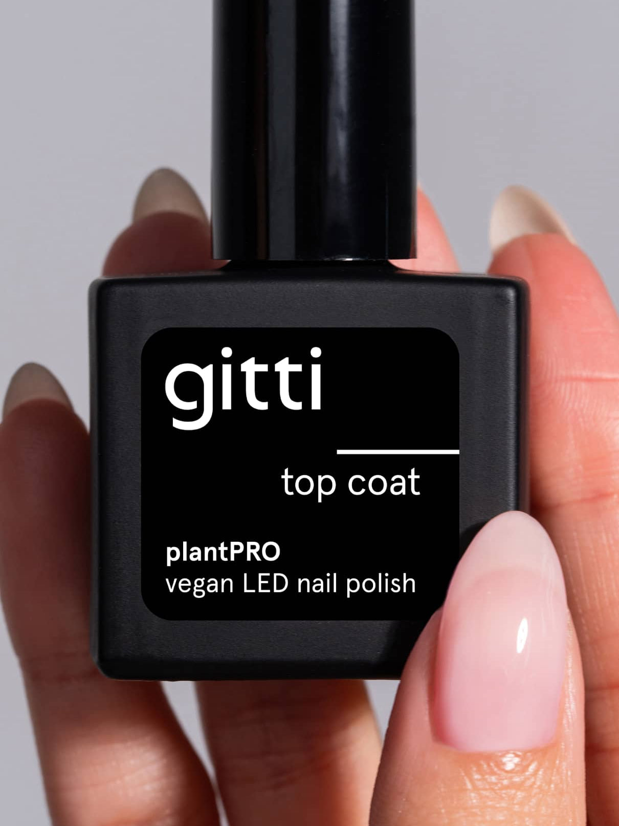Eine Hand mit manikürten Gelnägeln hält eine schwarze Flasche mit der Aufschrift plantPRO Top Coat, einem veganen LED-Nagellack auf Pflanzenbasis von gitti.