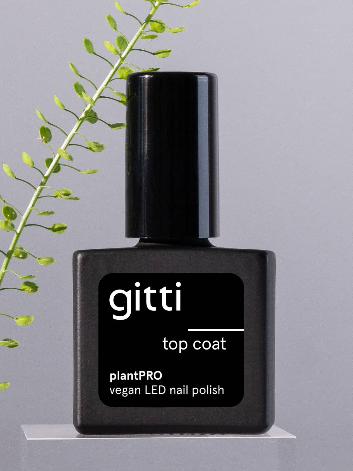 Eine schwarze Flasche plantPRO Top Coat ist mit einem grünen Pflanzenzweig im Hintergrund abgebildet, ideal für einen natürlichen Gelnagel-Look.