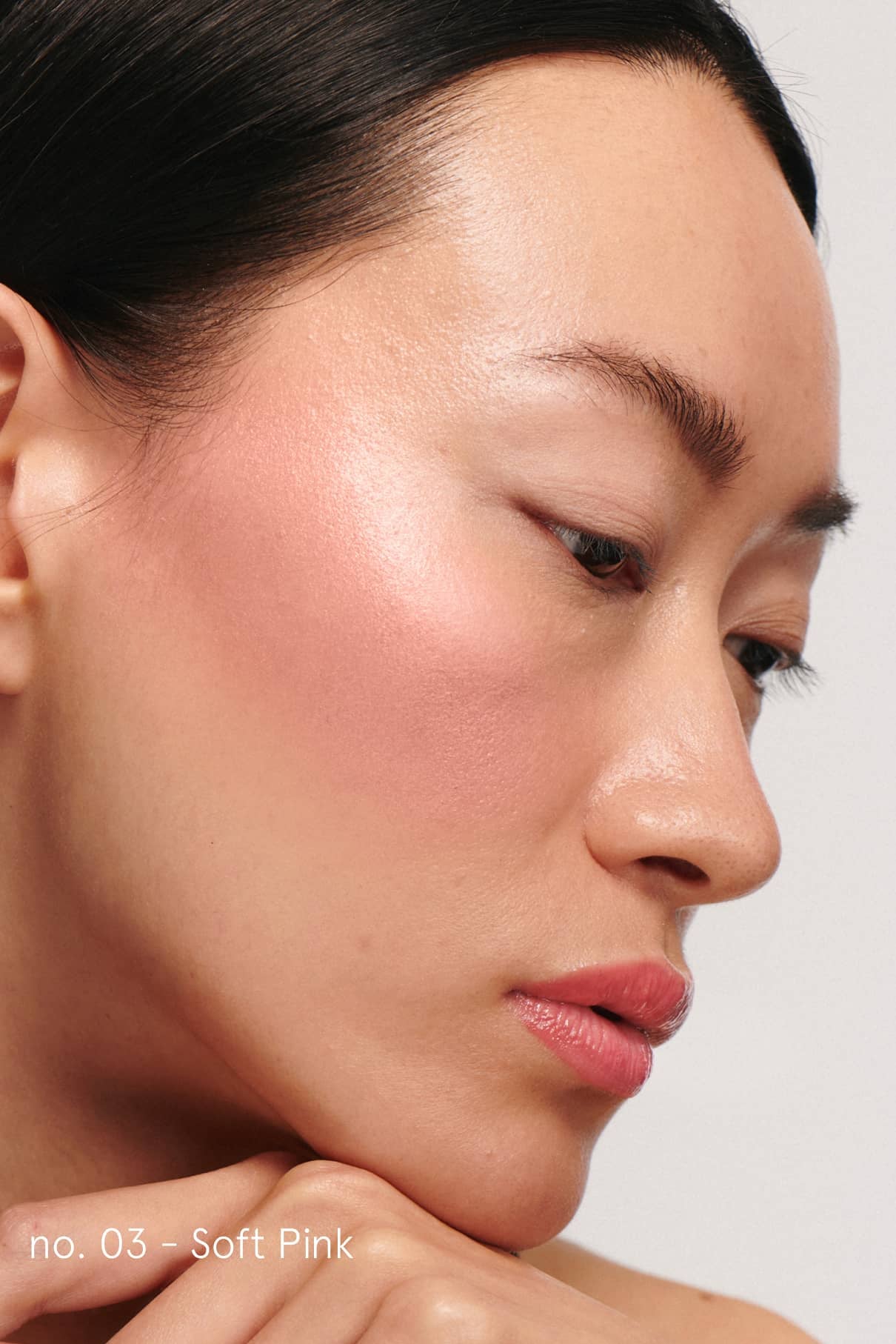 Eine Nahaufnahme zeigt glatte Haut mit zartrosa Rouge aus dem Cheek & Lash Duo auf der Wange und glänzenden rosa Lippen. In der unteren linken Ecke erscheint der Text "no. 03 - Soft Pink".