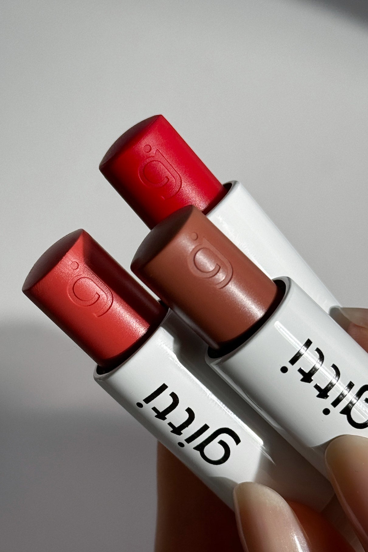 Drei Tuben mit rotem, pinkem und nudefarbenem Lippenstift befinden sich in einem weißen Etui mit Glitti-Branding und dem Nails + Lips in Sync-Design.