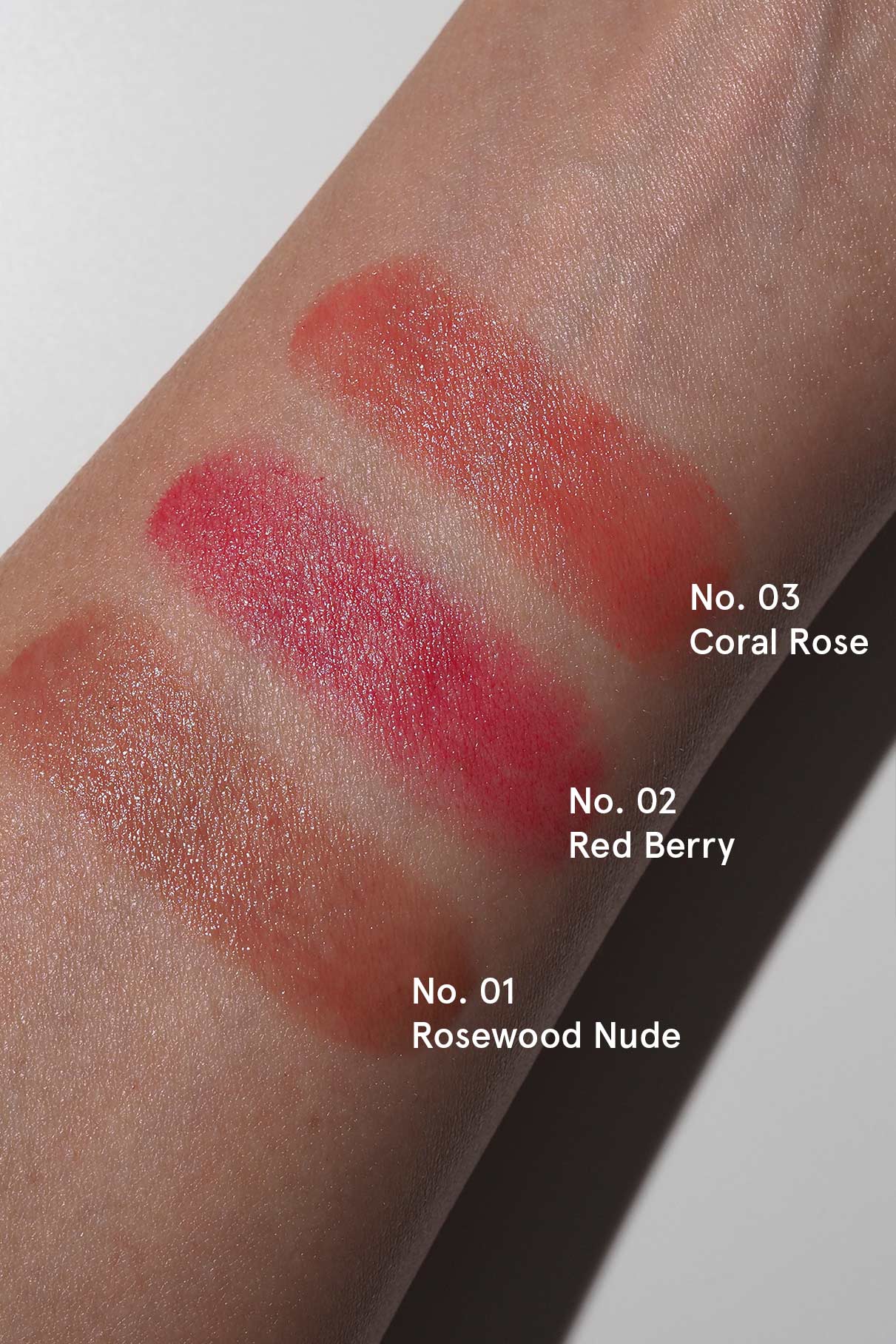 Drei Lippenstifte - Nr. 01 Rosewood Nude, Nr. 02 Red Berry und Nr. 03 Coral Rose - werden auf einem Unterarm präsentiert und passen perfekt zu allen Nails + Lips in Sync-Farbtönen für einen wunderbar abgestimmten Look.
