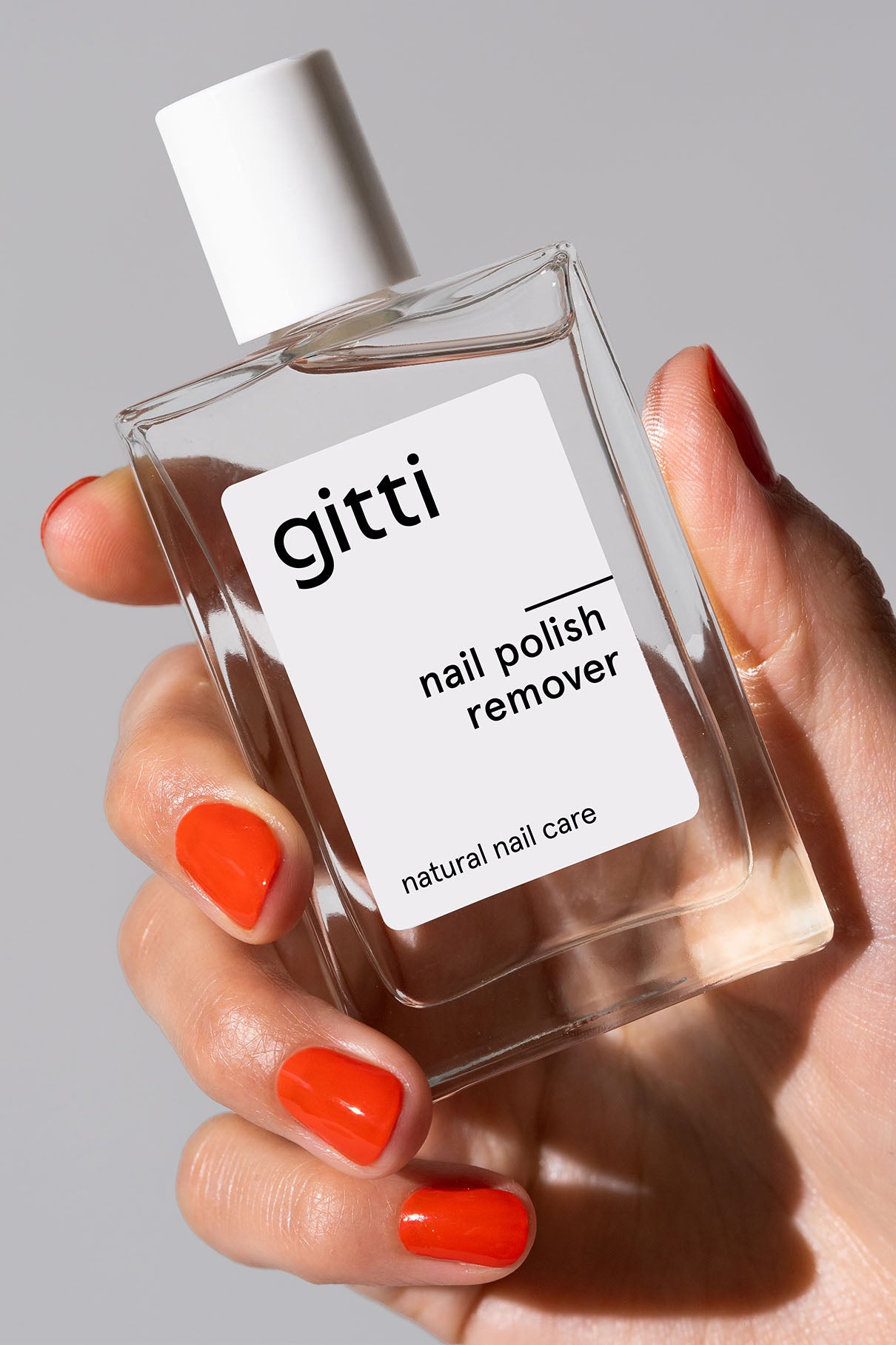 Eine Hand mit leuchtend orangefarbenem Nagellack hält eine klare rechteckige Flasche mit der Aufschrift Community Box, die unseren kostenlosen Versand vor einem schlichten Hintergrund hervorhebt.