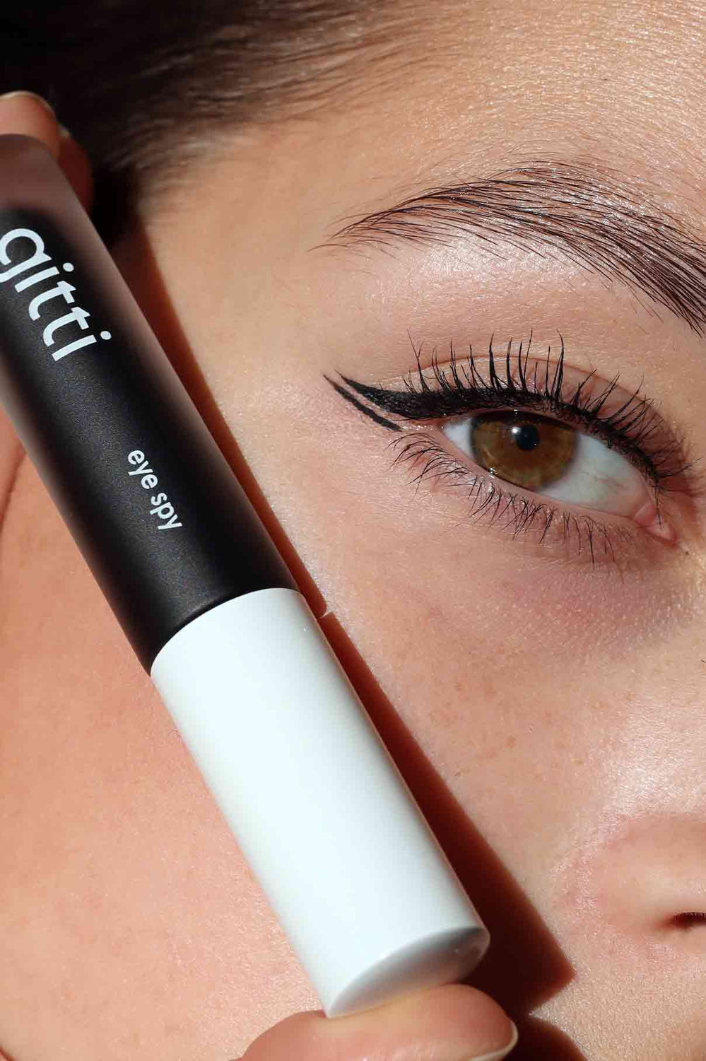 Nahaufnahme einer Person mit geflügeltem Eyeliner, die eine Tube aus der Community Box-jetzt als exklusives Set mit kostenlosem Versand erhältlich.