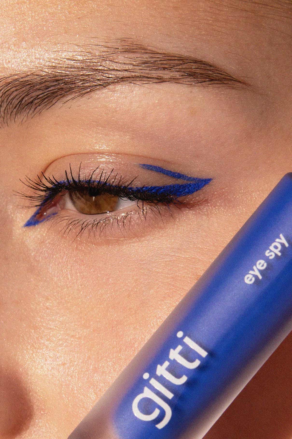 Nahaufnahme des Auges einer Person mit frechem blauen Wing-Eyeliner, die eine blaue Tube mit der Aufschrift gitti eye spy-die Community Box jetzt mit kostenlosem Versand und exklusivem Set erhältlich.
