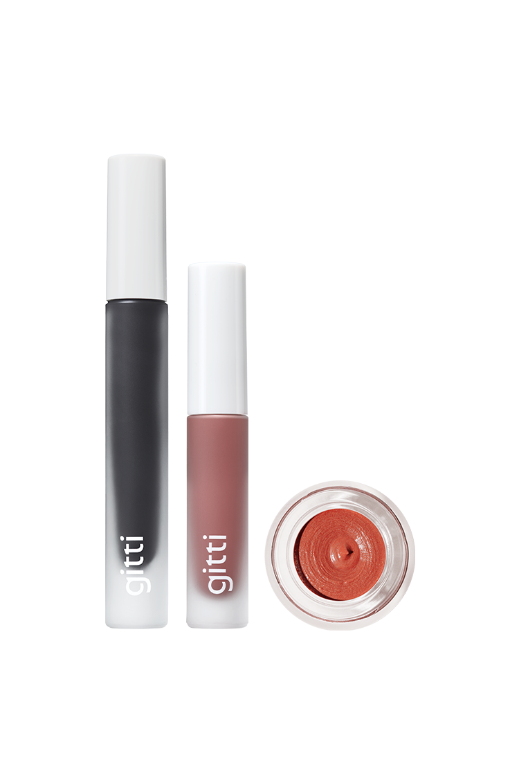 Das Lash, Lip & Cheek Trio besteht aus einer schwarzen Mascara-Tube, einem lilafarbenen Lip Glaze und einem geöffneten Tiegel mit terrakottafarben schimmerndem Velvet Cheeks Creme-Make-up, die alle auf einem weißen Hintergrund präsentiert werden.