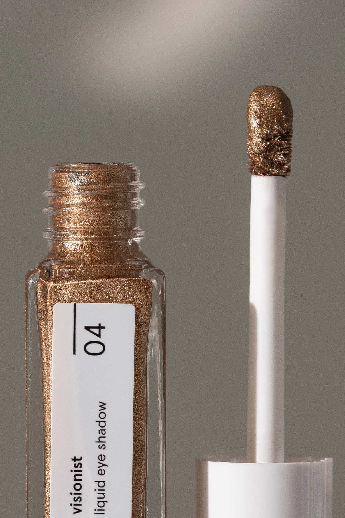 Eine Nahaufnahme der geöffneten Visionist No. 04 Tube zeigt den Applikator und den warmen Goldton im Inneren des transparenten Behälters. Dieser lang anhaltende flüssige Lidschatten sorgt für strahlende Farbe.
