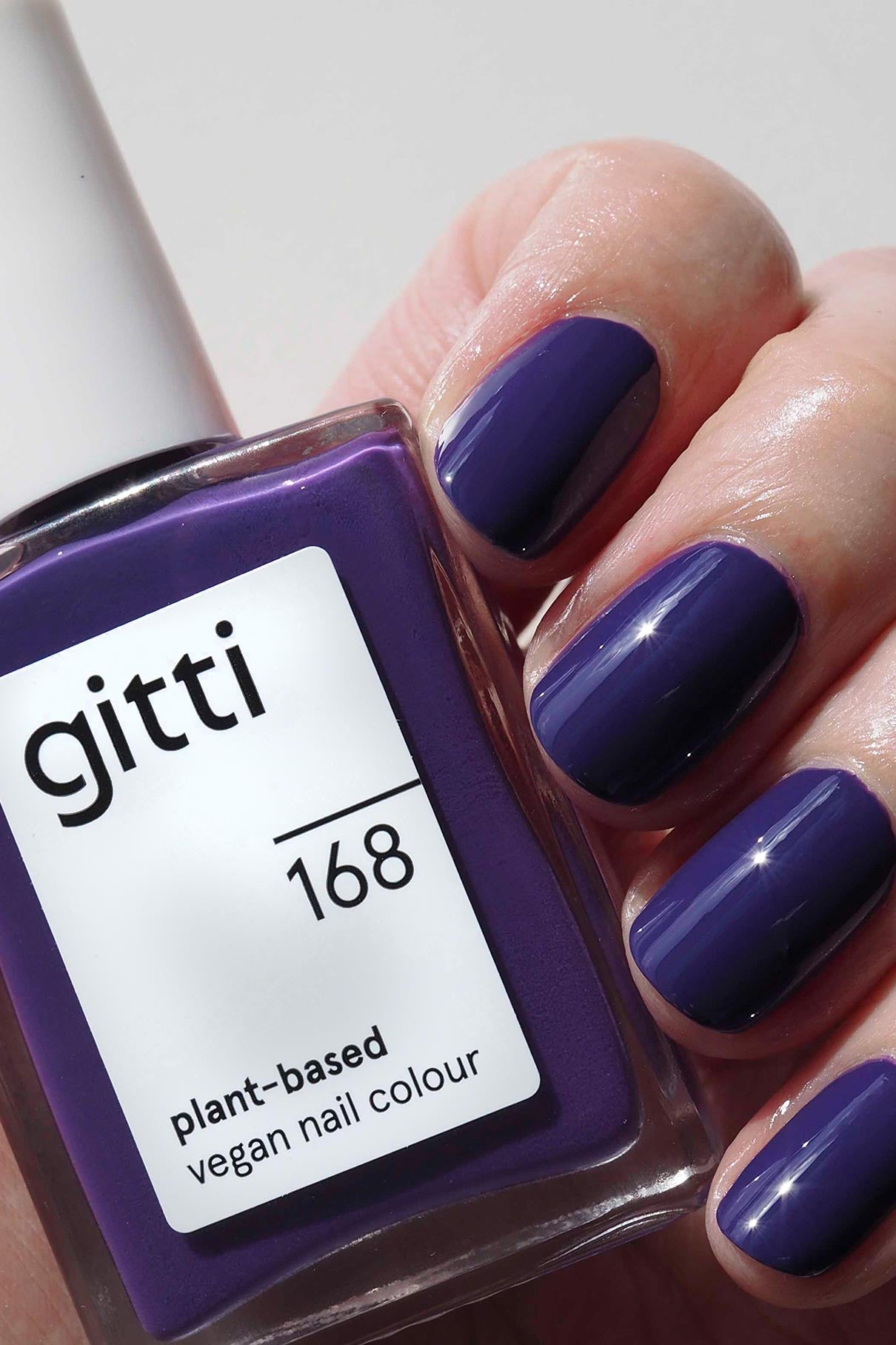 Eine Hand mit kurzen Nägeln, die mit pflanzlicher, veganer Nagelfarbe von Nails + Lips in Sync lackiert sind, hält den passenden Flakon, der das Set perfekt abrundet.