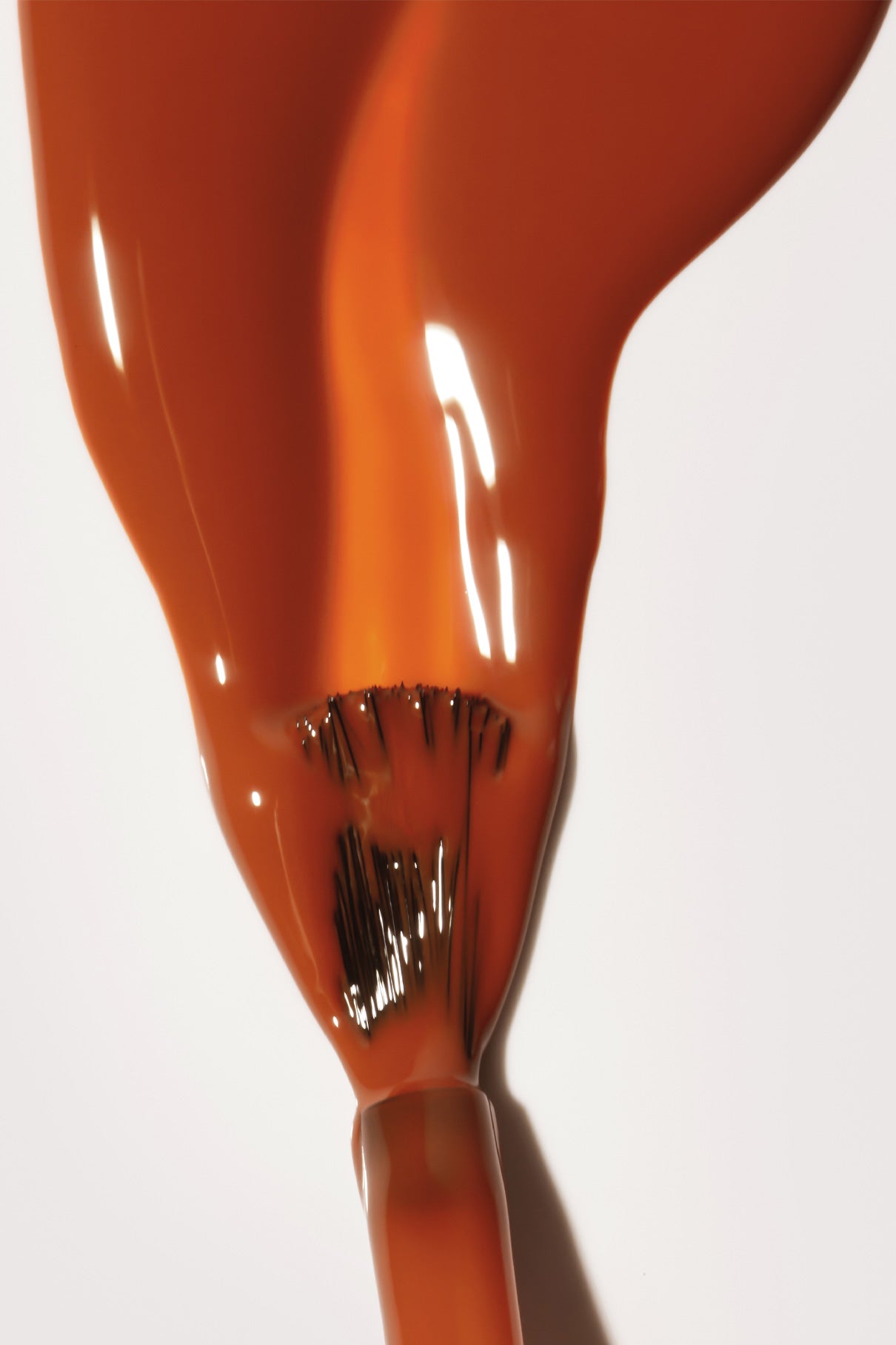 Nahaufnahme eines Pinsels, der Gitti Nr. 180, eine orange-braune Farbe, gleichmäßig auf eine glänzende weiße Oberfläche auf.