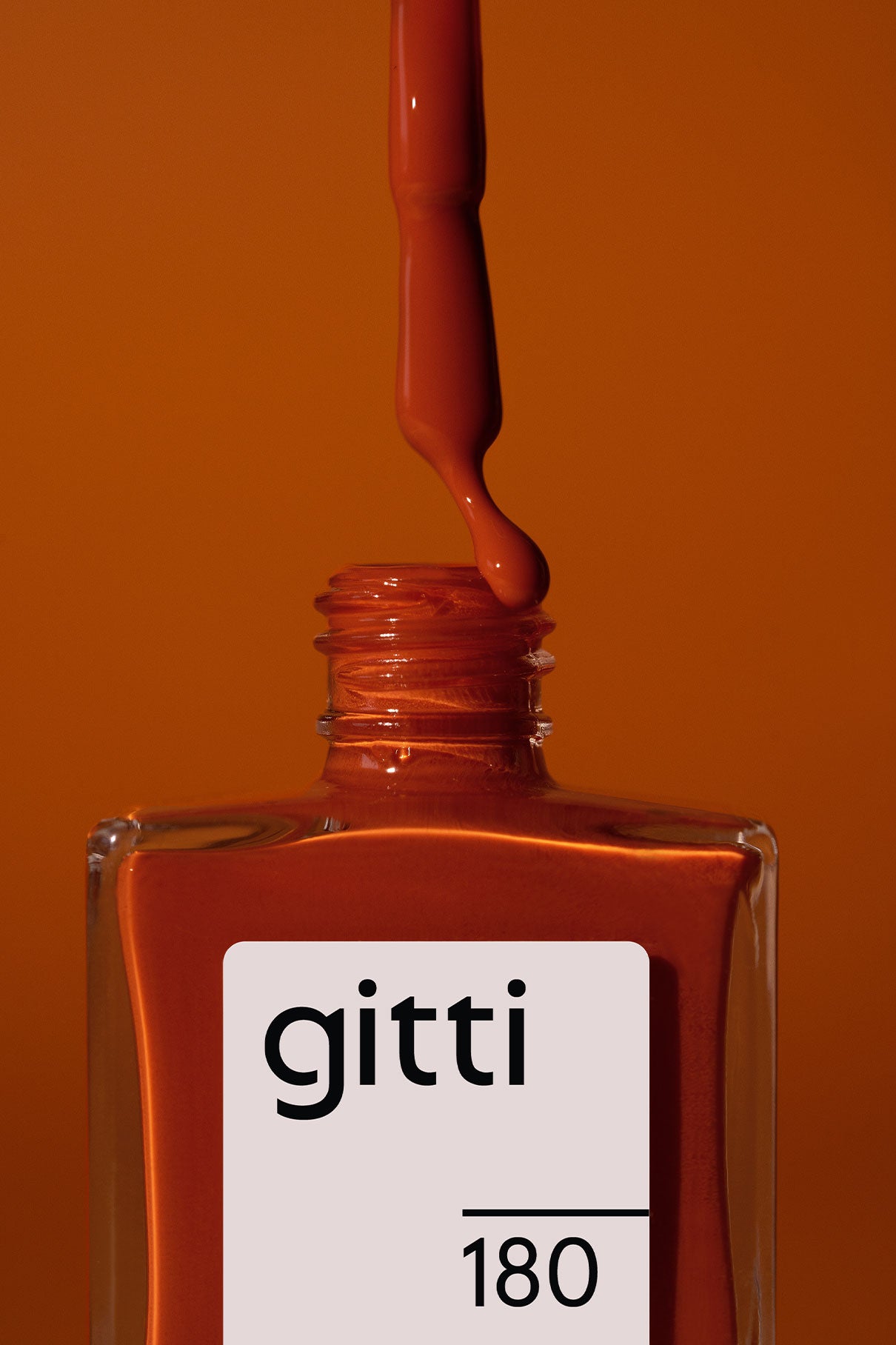 Eine Flasche gitti no. 180 Nagellack mit dem Pinsel über die offene Flasche gehalten, tropft Sattes Orangebraun Schatten vor einem orangefarbenen Hintergrund.