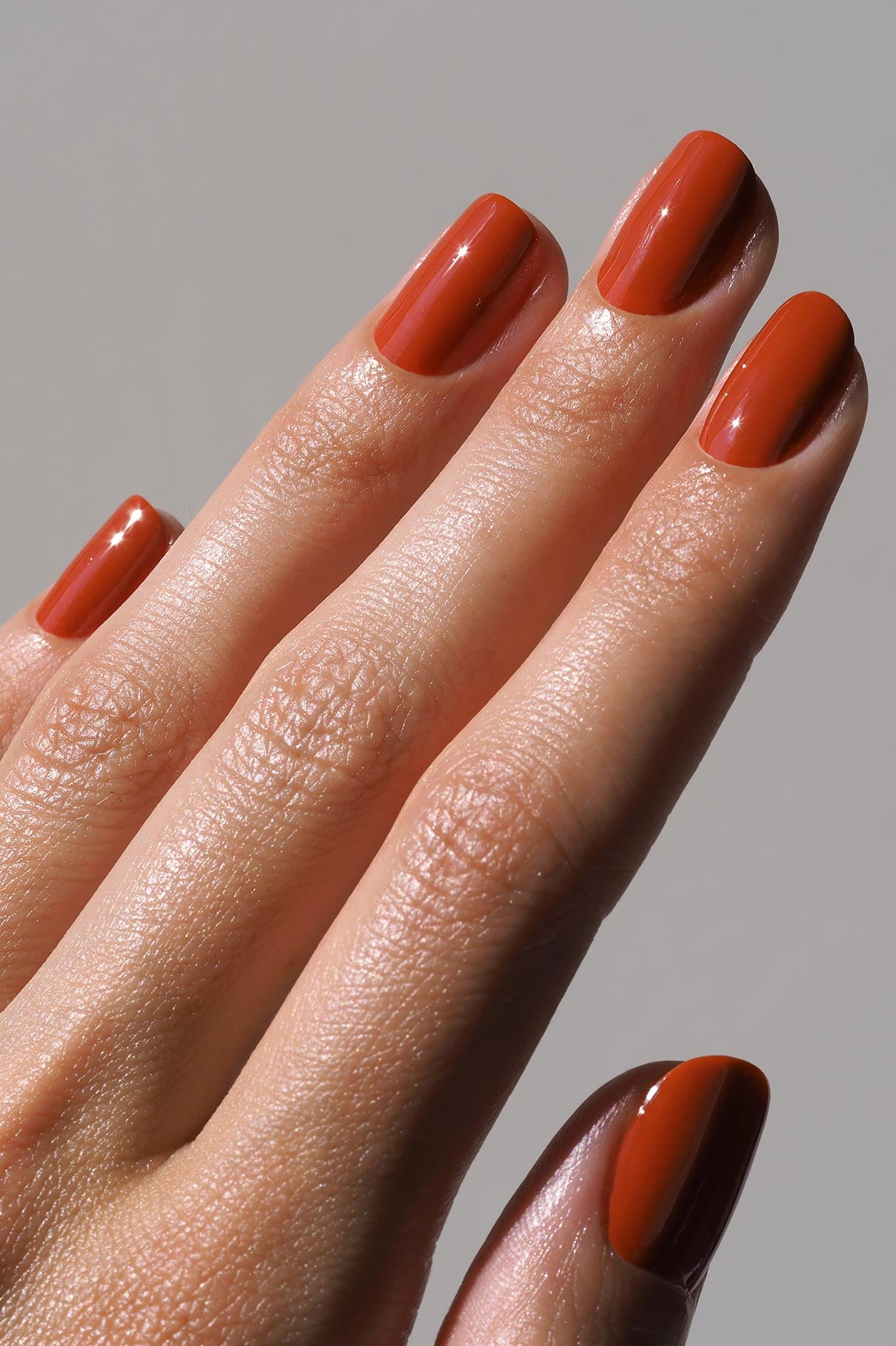 Nahaufnahme einer Hand mit sauber manikürten Nägeln, die mit glänzendem, sattem Orangebraun gitti no. 180 Lack lackiert sind.