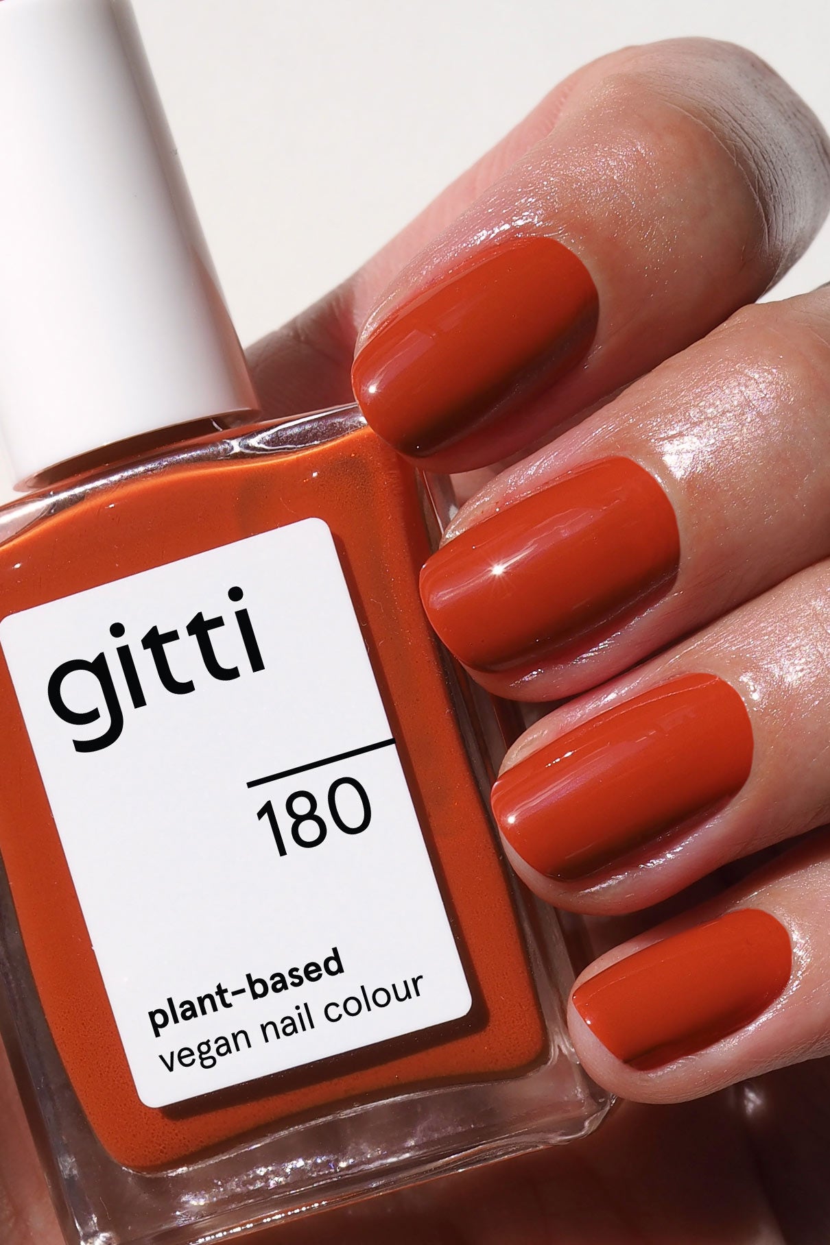 Eine Hand mit sauber manikürten, in sattes Orangebraun lackierten Nägeln hält eine Flasche gitti no. 180, einem veganen Nagellack auf Pflanzenbasis.