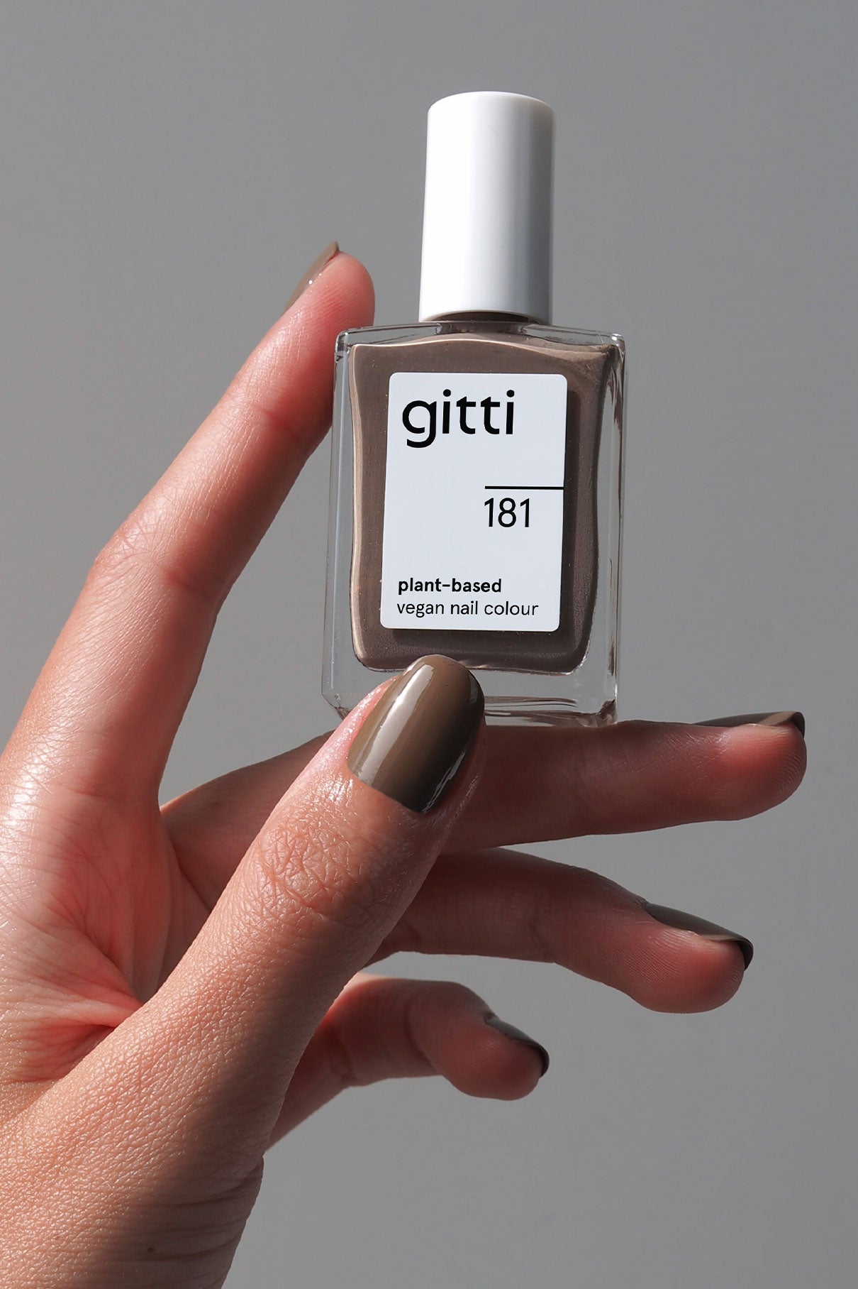 Eine Hand hält eine Flasche von gitti no. 181, einer pflanzlichen, veganen Nagelfarbe. Die Nägel sind in einem passenden Taupe-Grau mit dezentem Unterton lackiert.