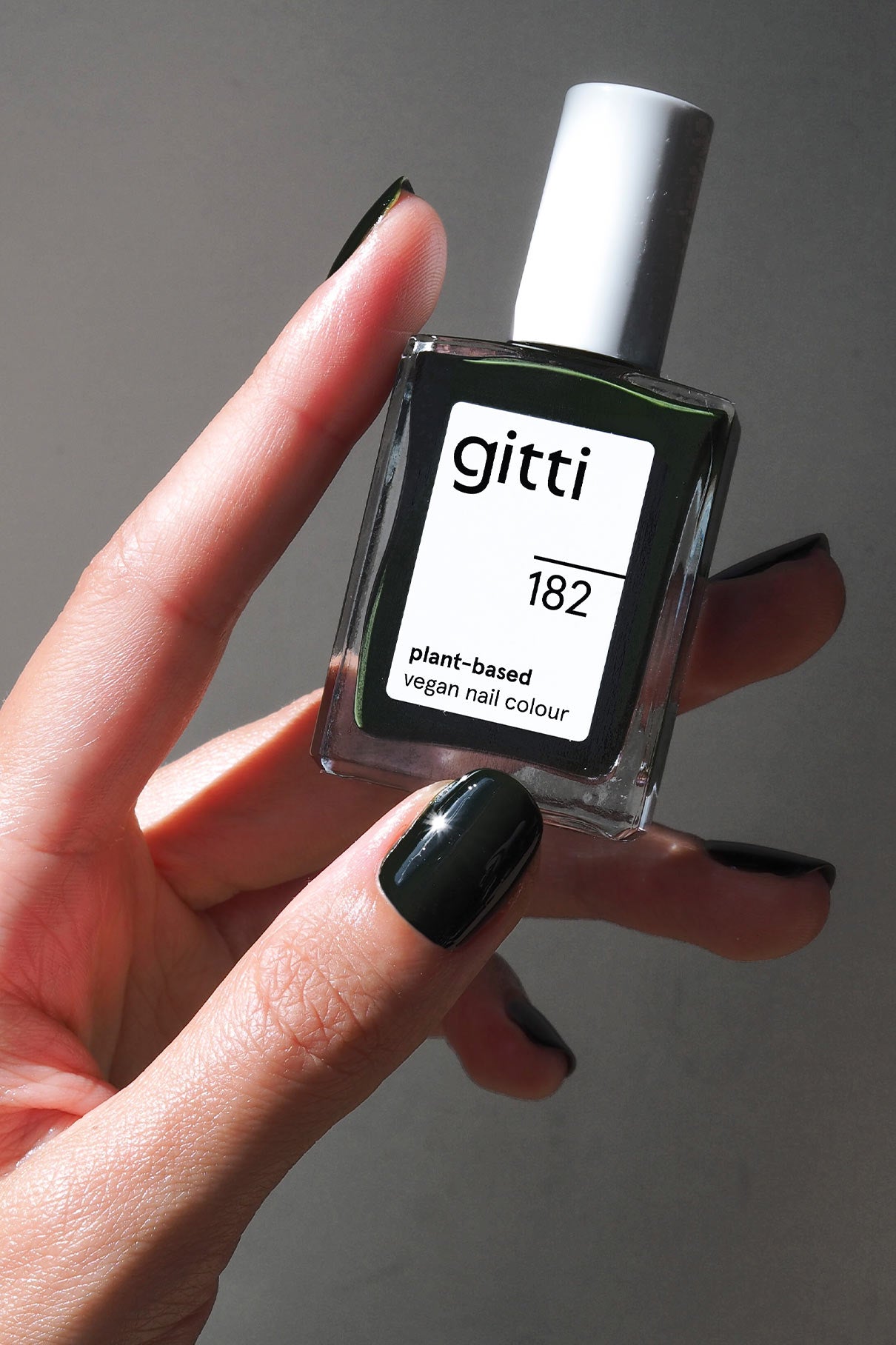 Eine Hand mit dunkelgrün lackierten Nägeln hält ein Fläschchen mit gitti no. 182 pflanzlicher veganer Nagelfarbe in dunklem Tannengrün.